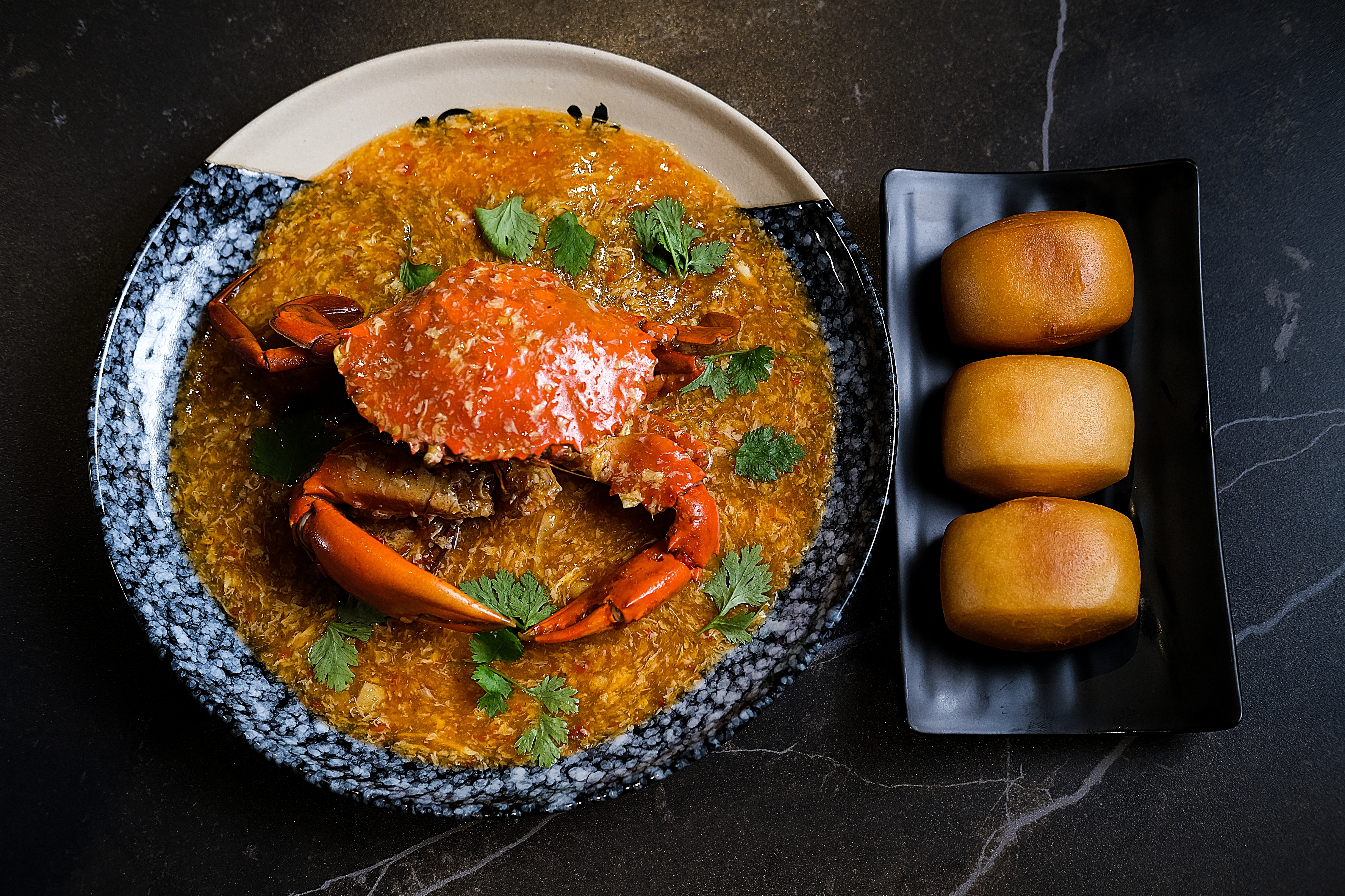 A plate of singaporean chili  crab. The crab is sitting on a sauce. There is also a piece of mantou bread on the right side of the plate