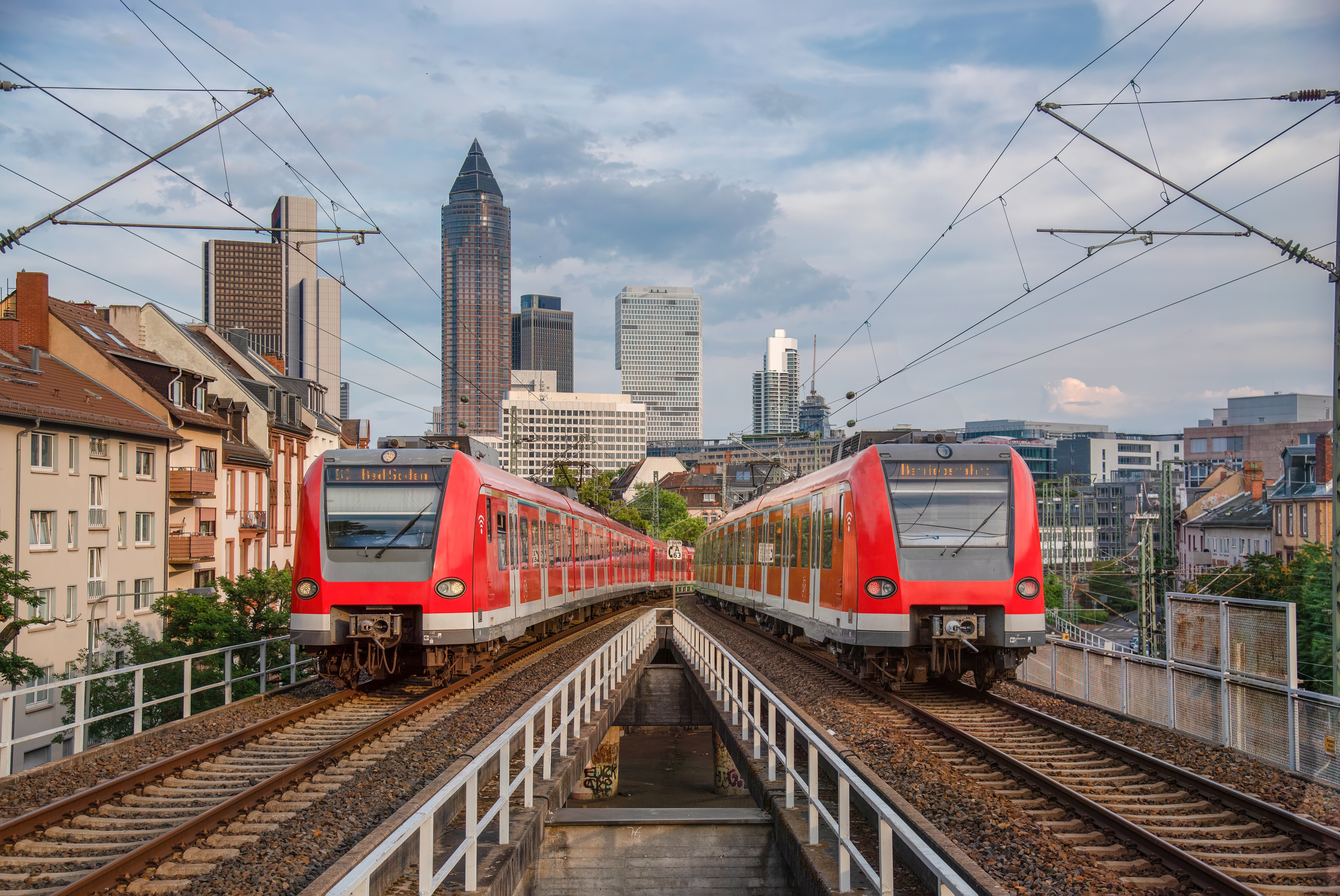 Under Frankfurt's bustling skyline, two red trains enter the station. The rhythm of urban life and the steady movement of trains intersect, showcasing the power and speed of German city transport.
