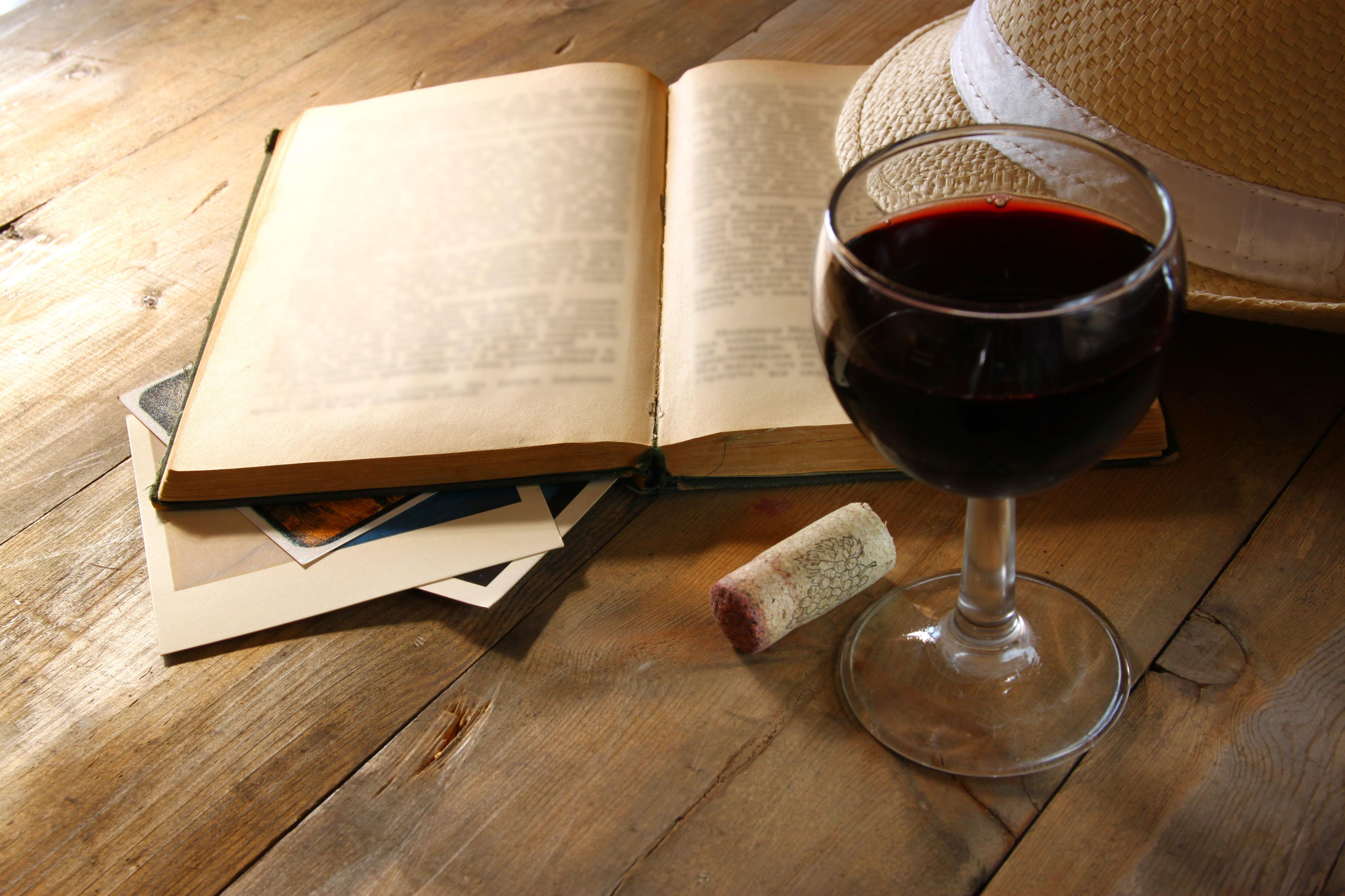 Red wine glass and old open book on wooden table at sun burst. vintage filtered image