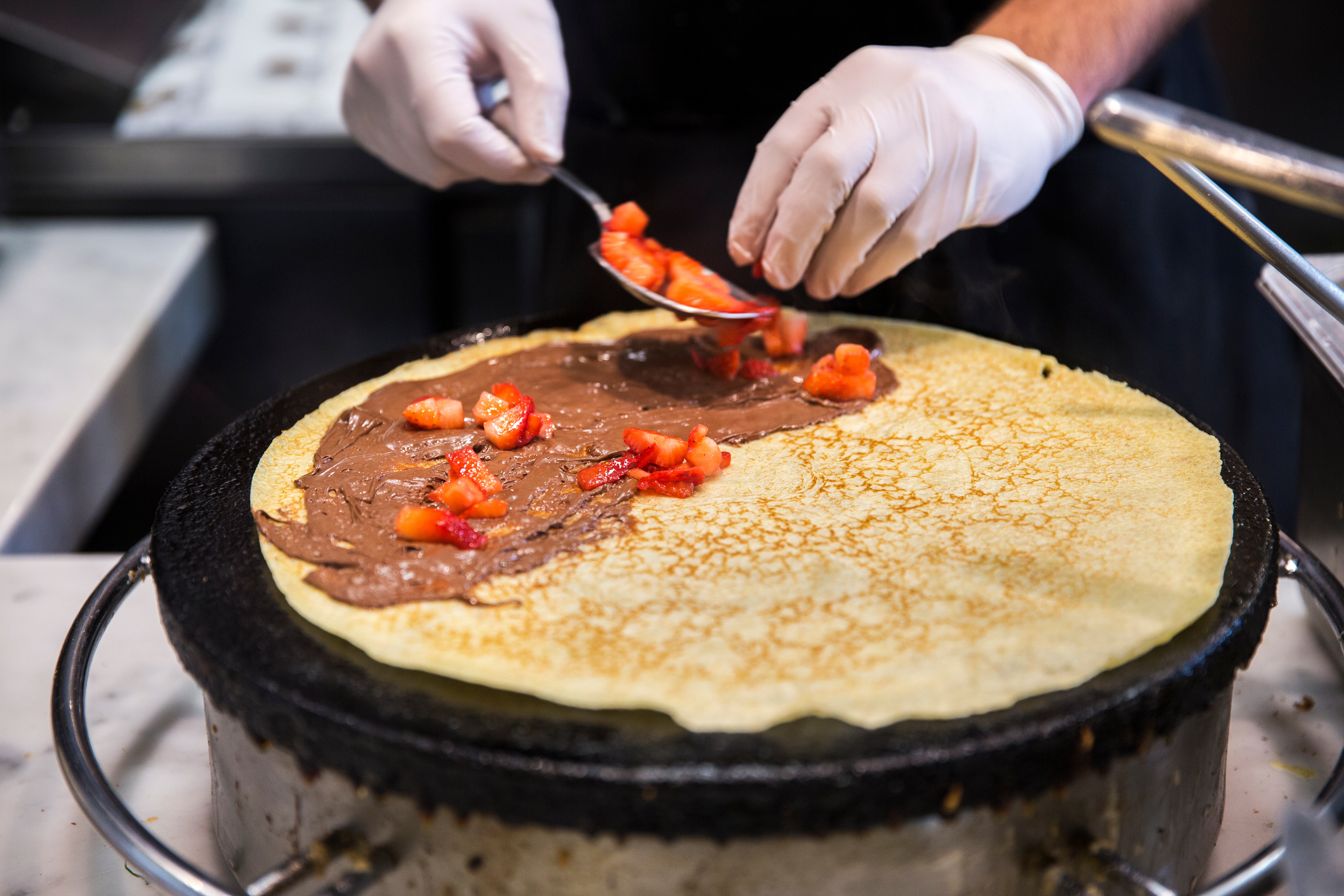 Chocolate Strawberry Crepe being Prepared by Hand with Hazelnut Syrup on Skillet Topped with Fresh Berries at European Creperie