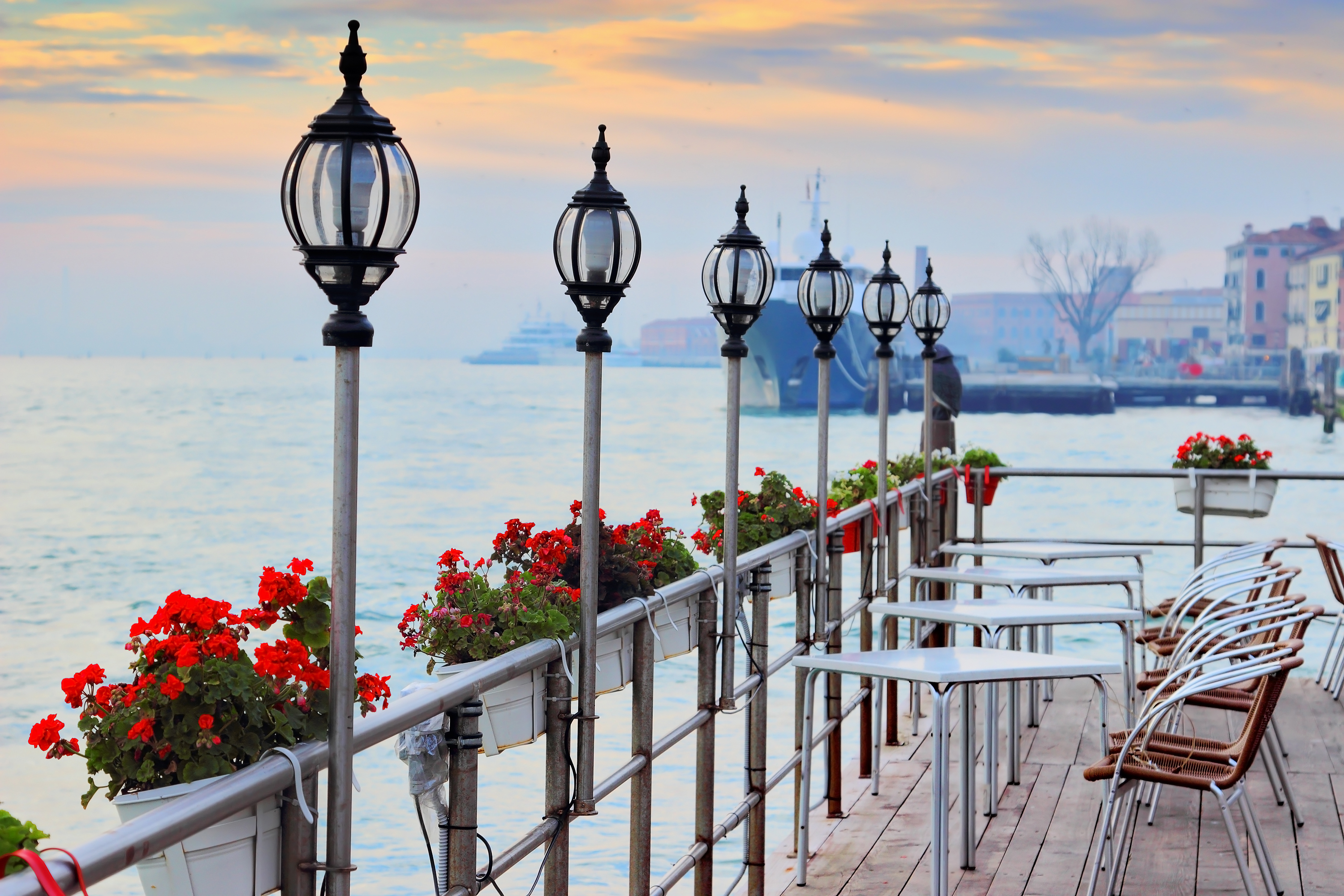 Street open cafe with view at the canal, Venice, Italy. Tables and seats are empty. Flowers decorate cafe. Cozy romantic evening place.