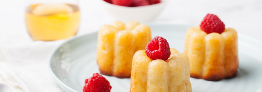 French dessert, cakes, caneles, rum baba with fresh raspberry and dessert wine on a white background