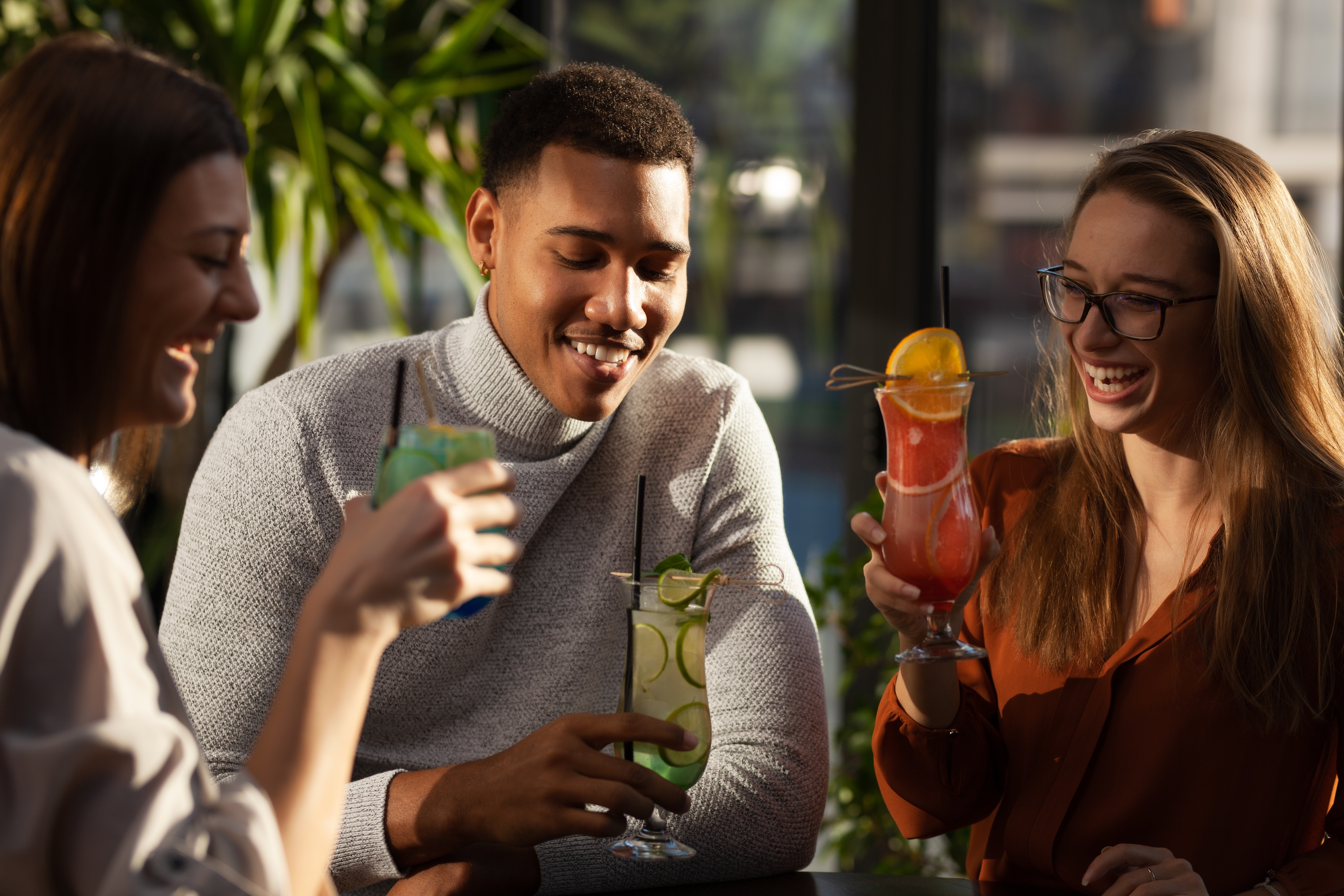 Three multiracial friends in a bar cheering. After work party with cocktails after successful work day.
