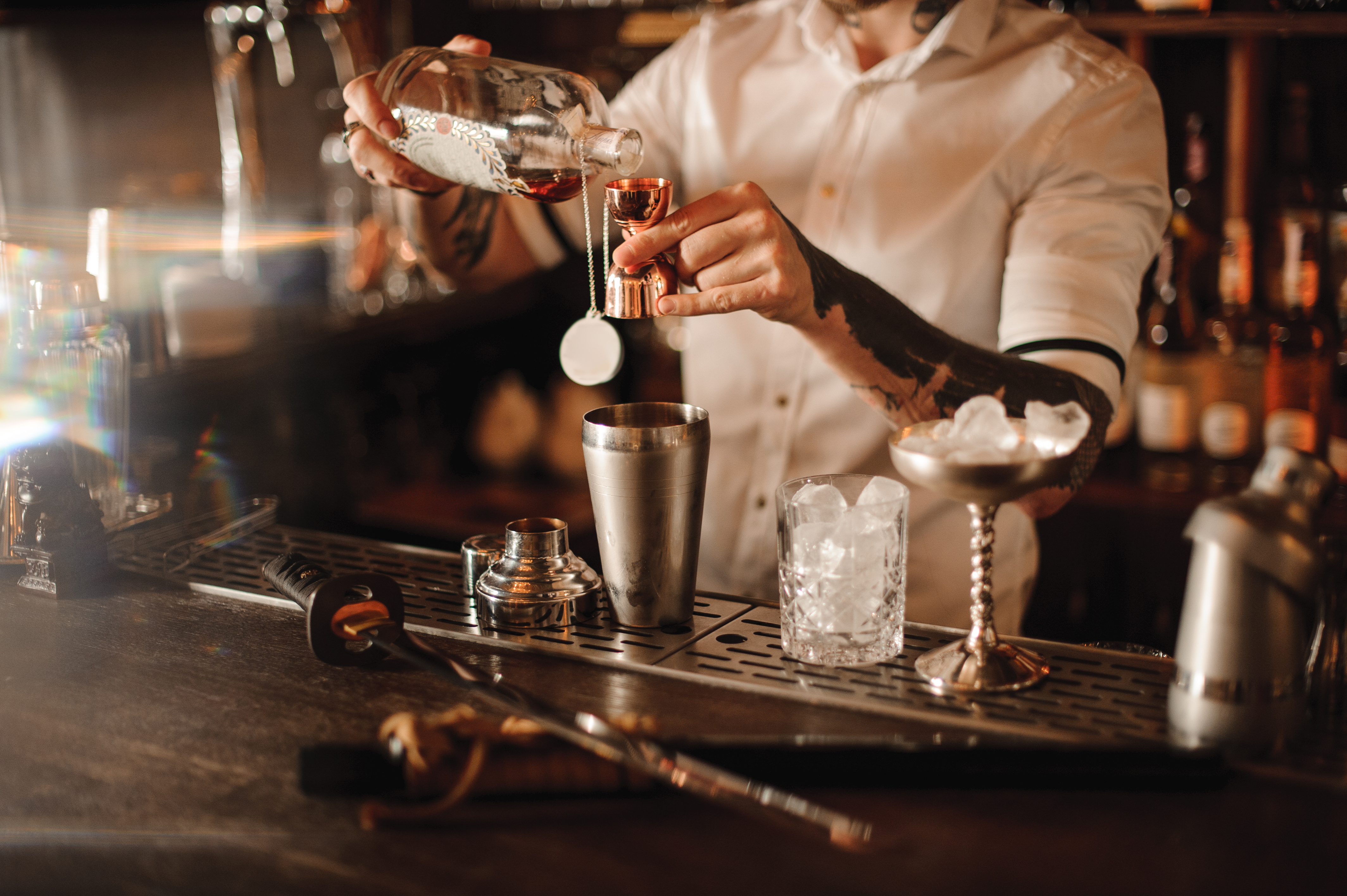 Bartender is adding ingredient in shaker at bar counter