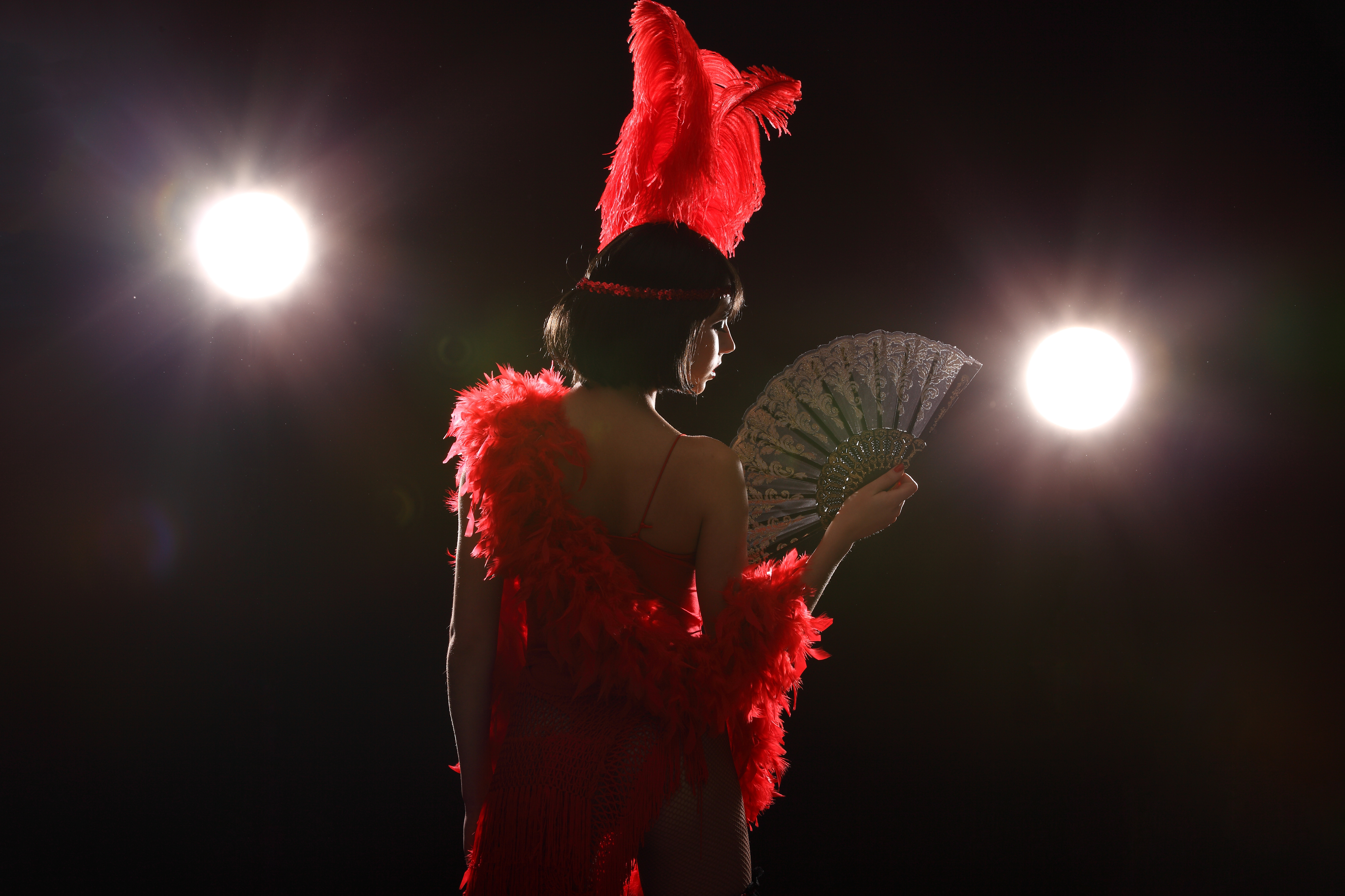 Burlesque dancer with red plumage and red short dress, black and red background, on the stage