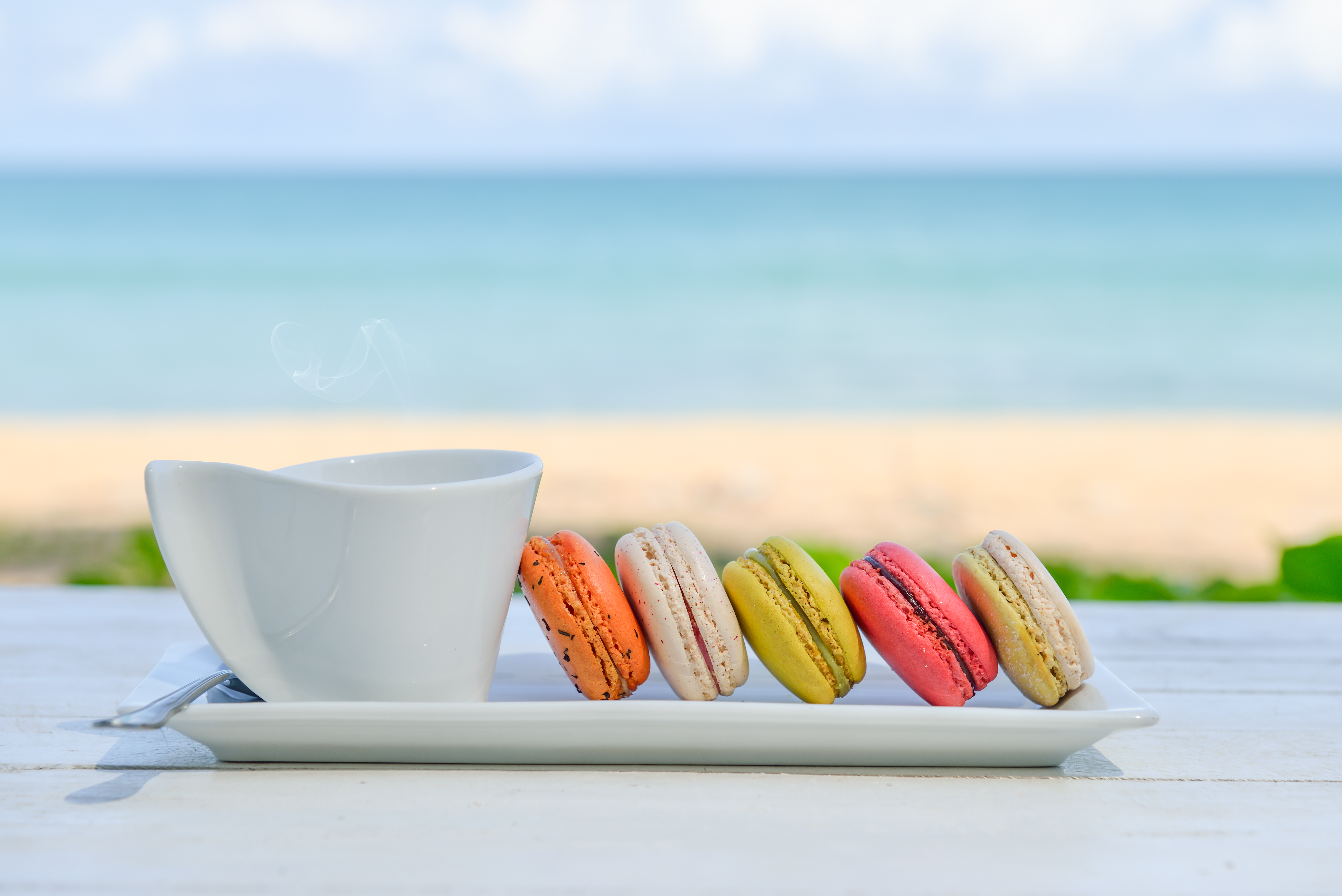 macaroon multicolored with a cup of coffee on white table with sea and blue sky background