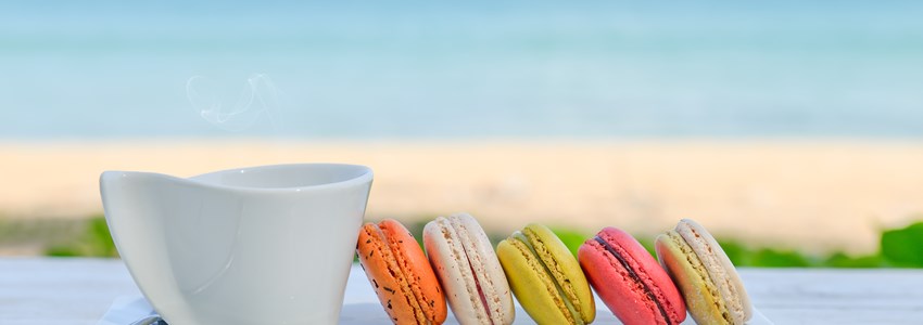 macaroon multicolored with a cup of coffee on white table with sea and blue sky background