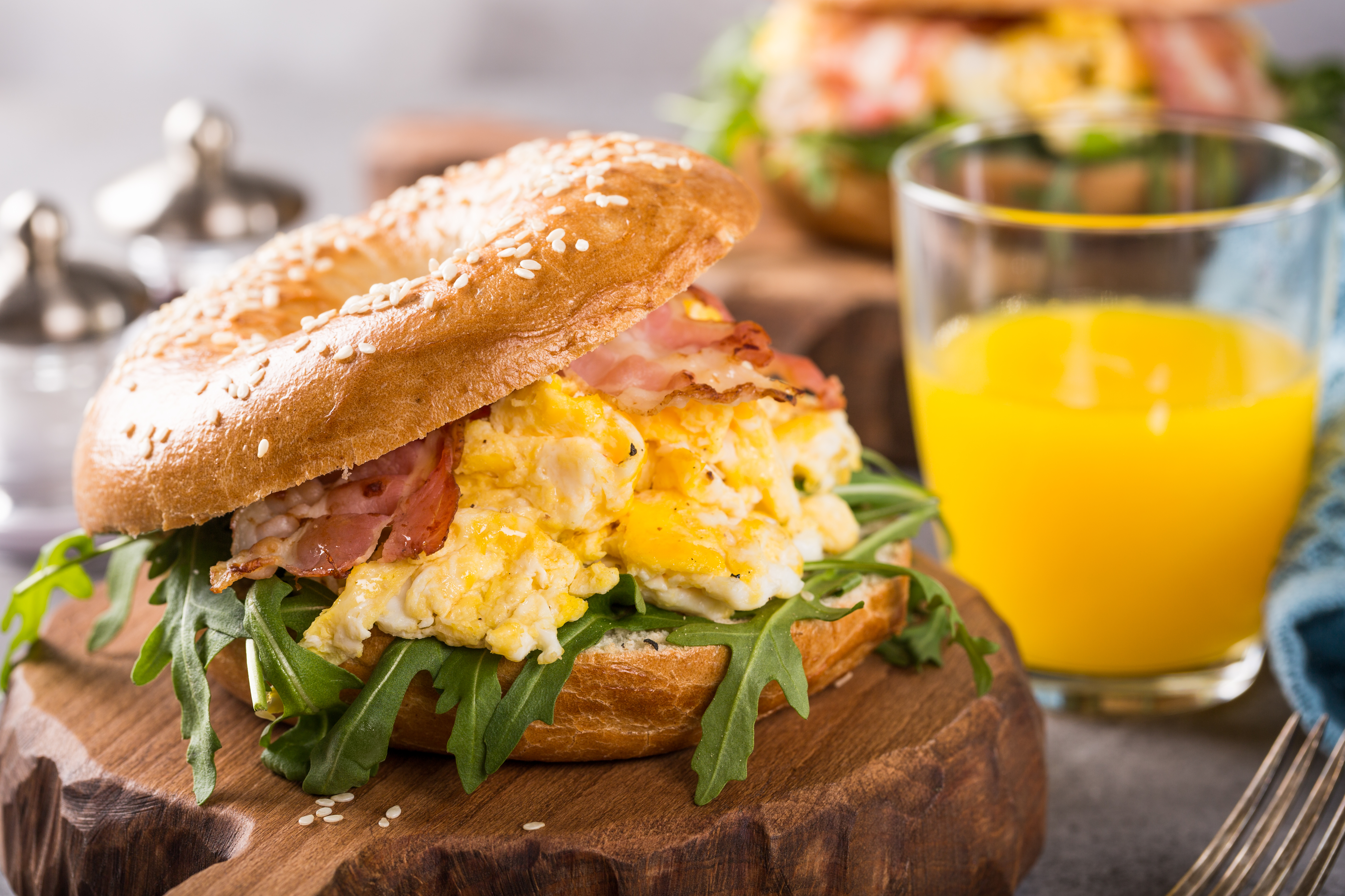 Healthy freshly baked bagel filled with scrambled eggs, rucola and fried bacon
