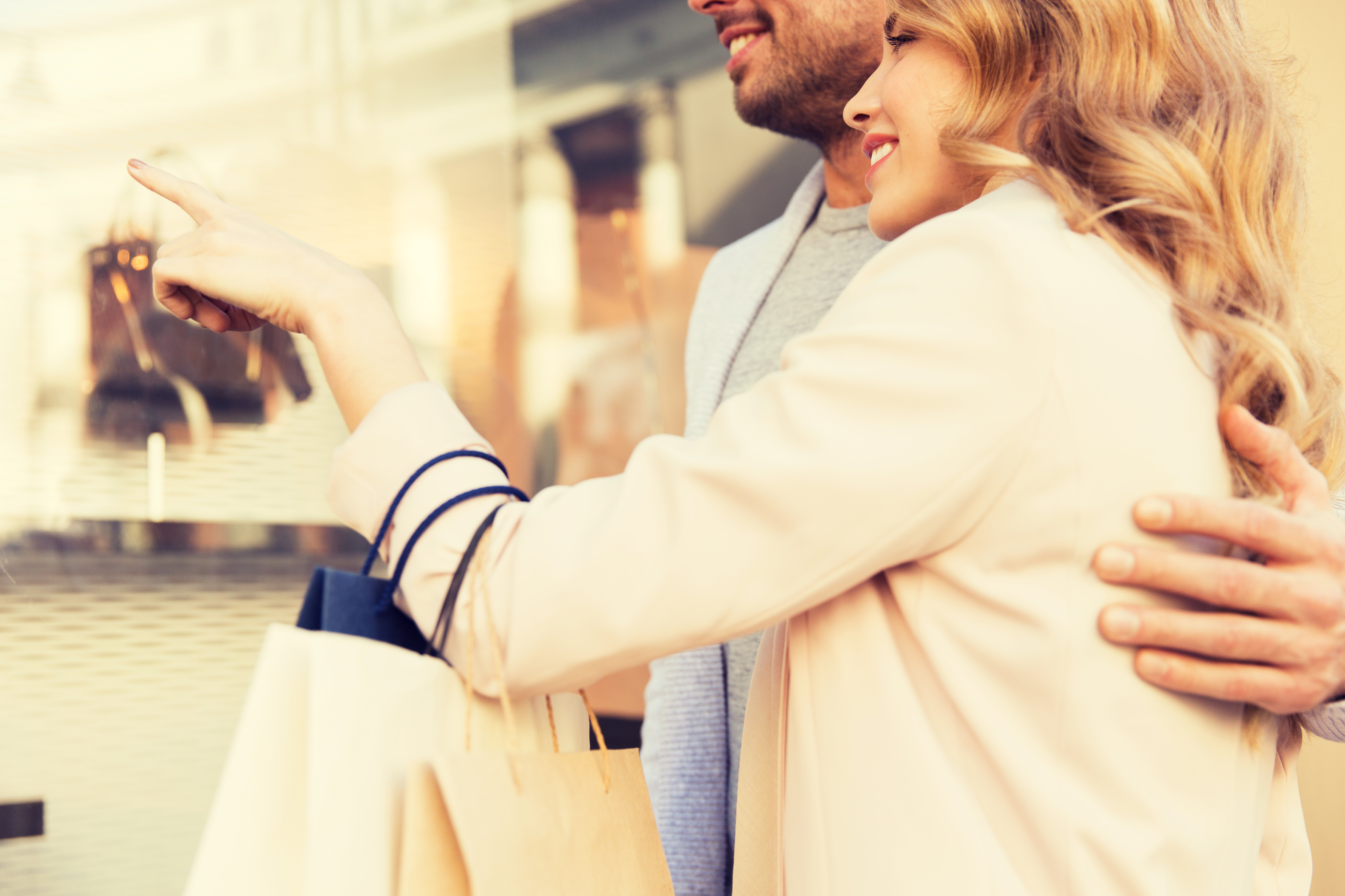 sale, consumerism and people concept - close up of happy couple with shopping bags looking at shop window in city