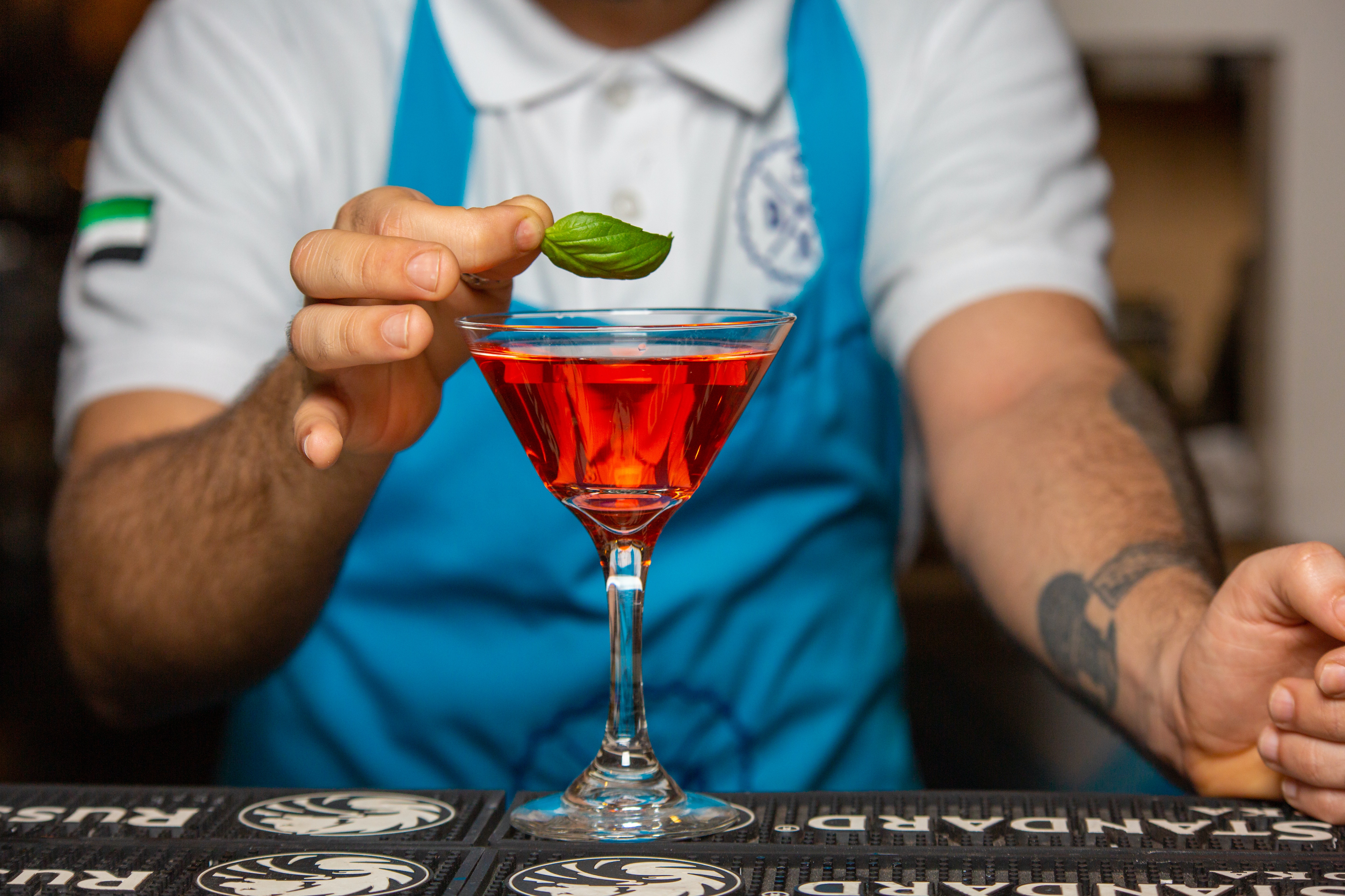 bartender finishing a red cocktail with a leaf of basil