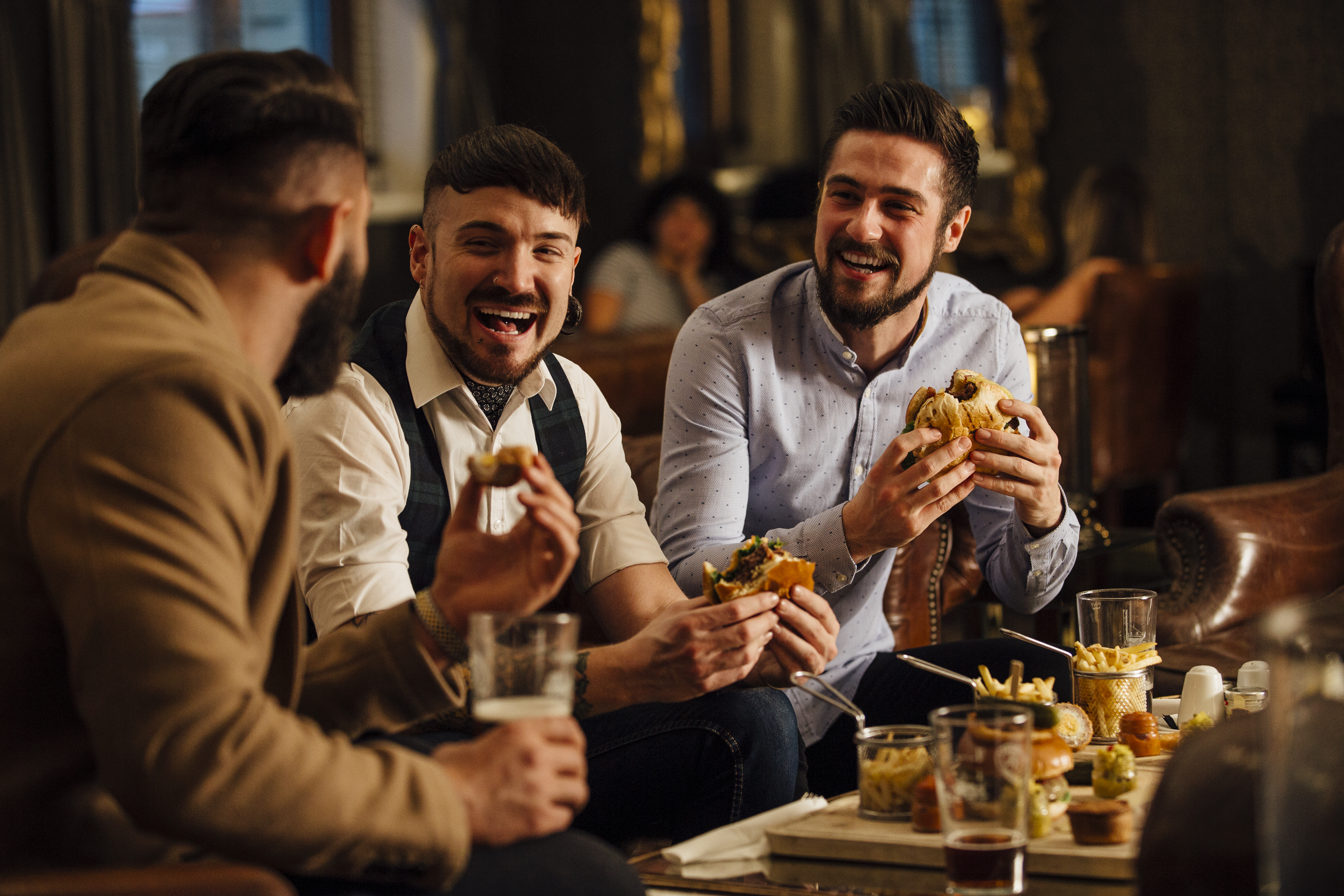 Three men sitting together in a bar/restaurant, talking while enjoying burgers and beer.