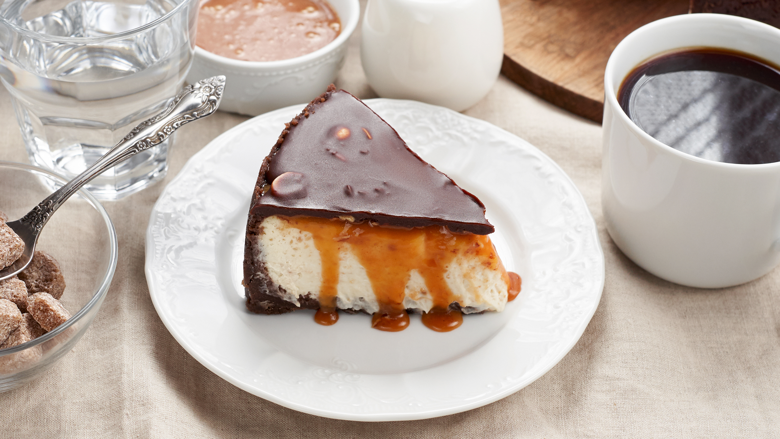 Close up view of a piece of Peanut Butter Chocolate Caramel Cheesecake Pie and cup of coffee on dining table with linen tablecloth. A Sweet Coffee Break concept