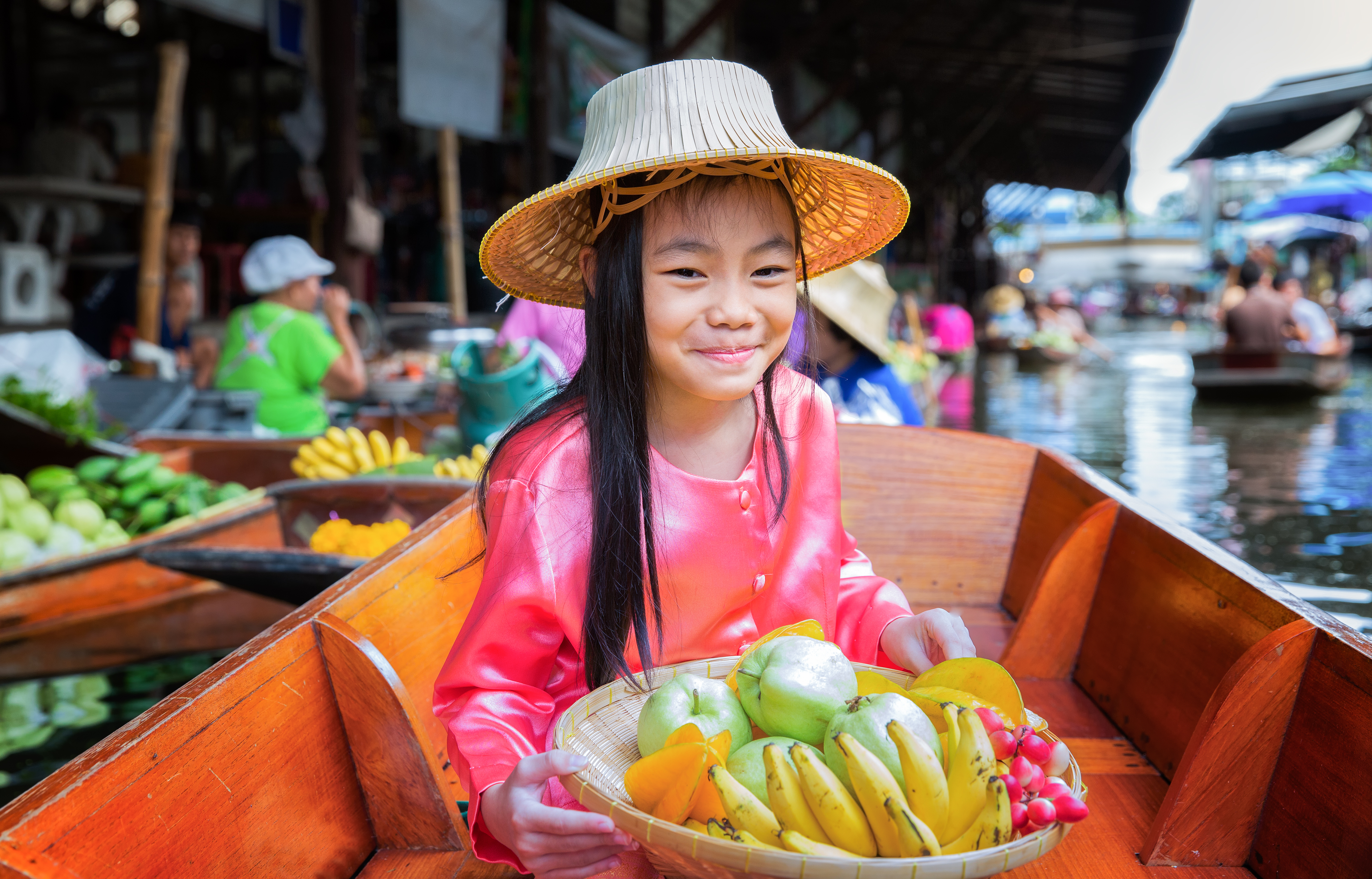 A child sits on the boat and holds a fruit basket in the traditional floating market in Bangkok, Thailand.