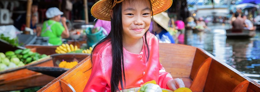 A child sits on the boat and holds a fruit basket in the traditional floating market in Bangkok, Thailand.