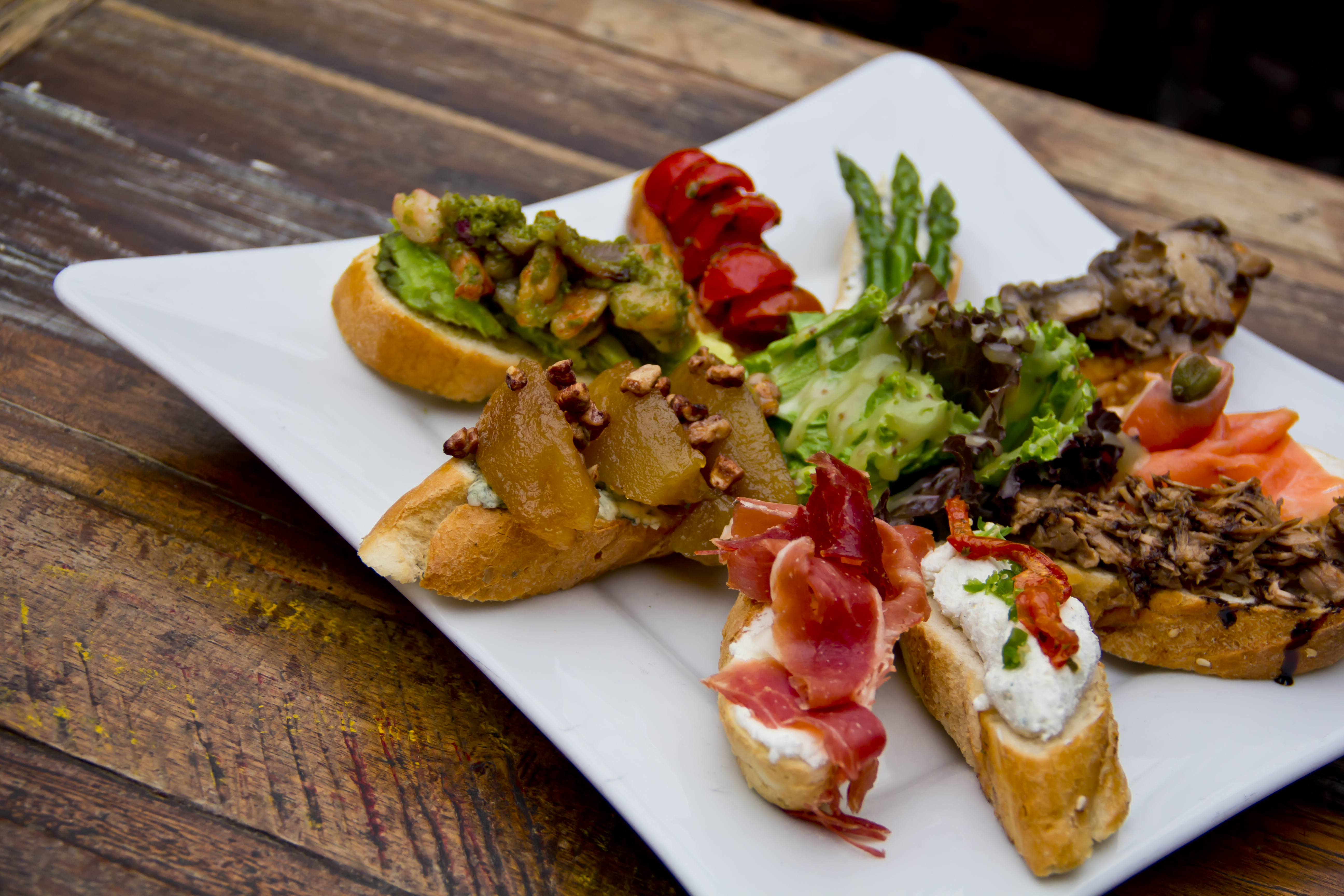 Spanish tapas assortment platter over a ceramic plate on a wooden table, top view.