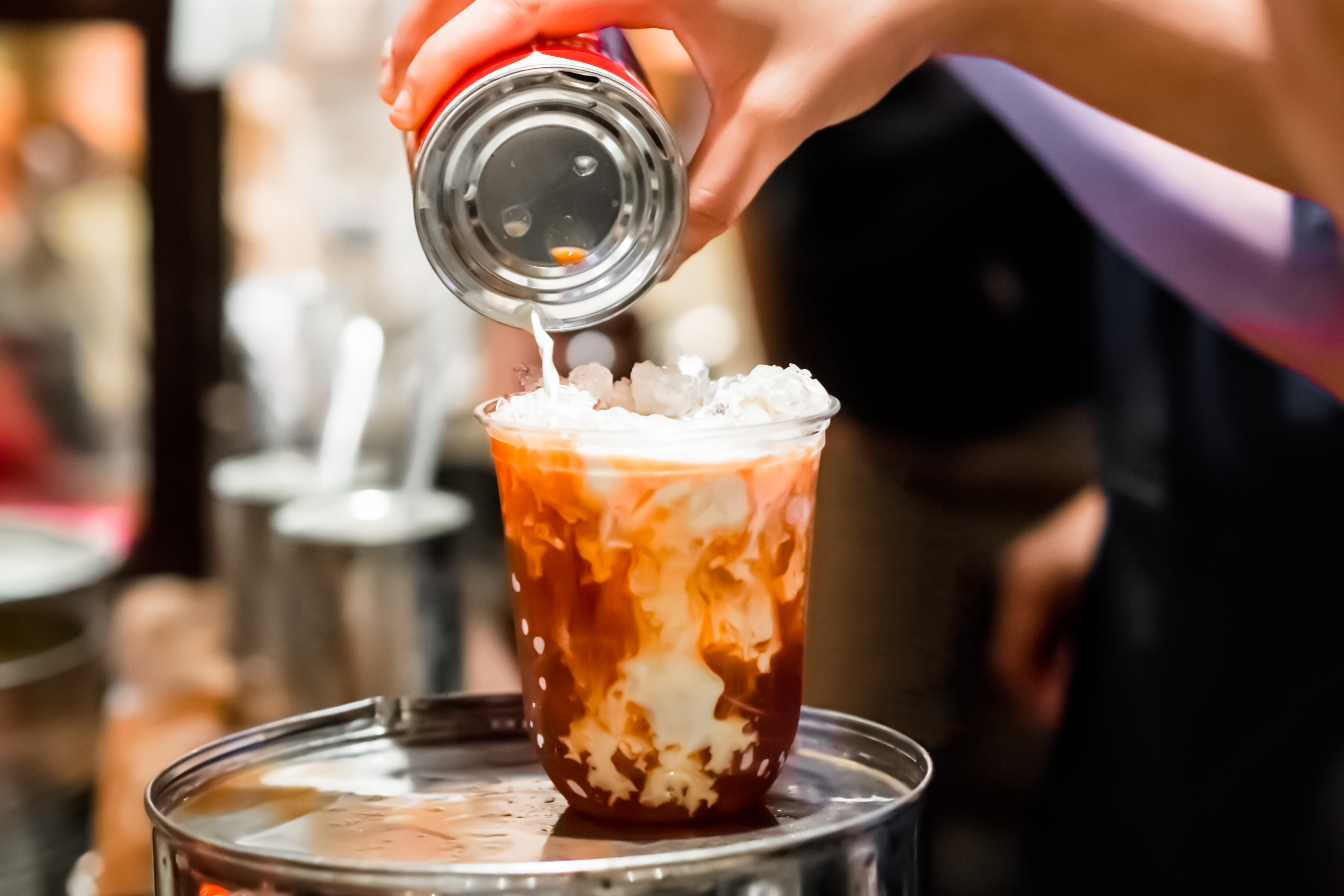 Thai orange traditional milk tea, Thailand local drink. Vintage coffee shop cafe in Southeast Asia. People making iced milk tea, pouring milk from tin can. Contrast marble texture between milk and tea