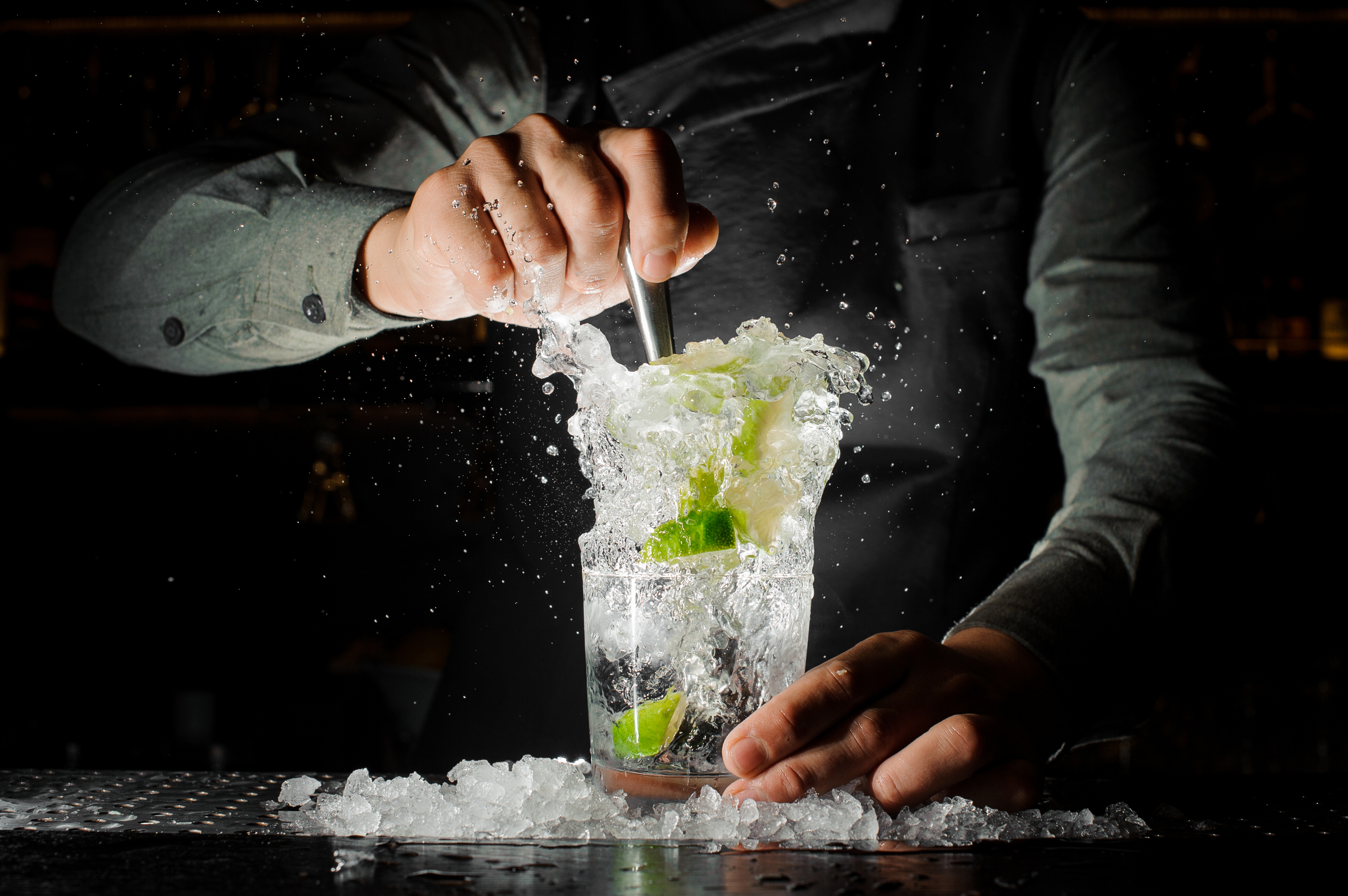 Bartender squeezing juice from fresh lime in a glass using a citrus press and splashing it out making an alcoholic cocktail