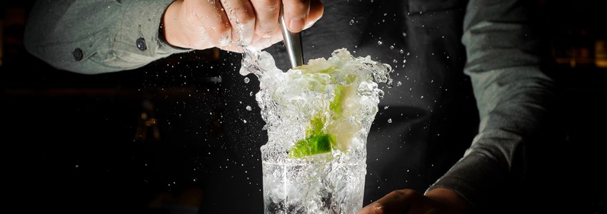 Bartender squeezing juice from fresh lime in a glass using a citrus press and splashing it out making an alcoholic cocktail