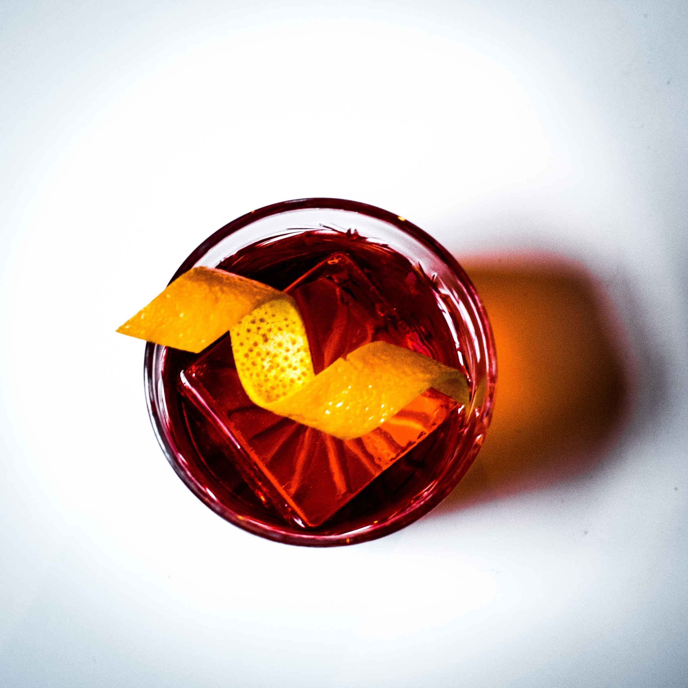 Top-down view of a Negroni cocktail with a clear ice cube and an orange peel twist garnish