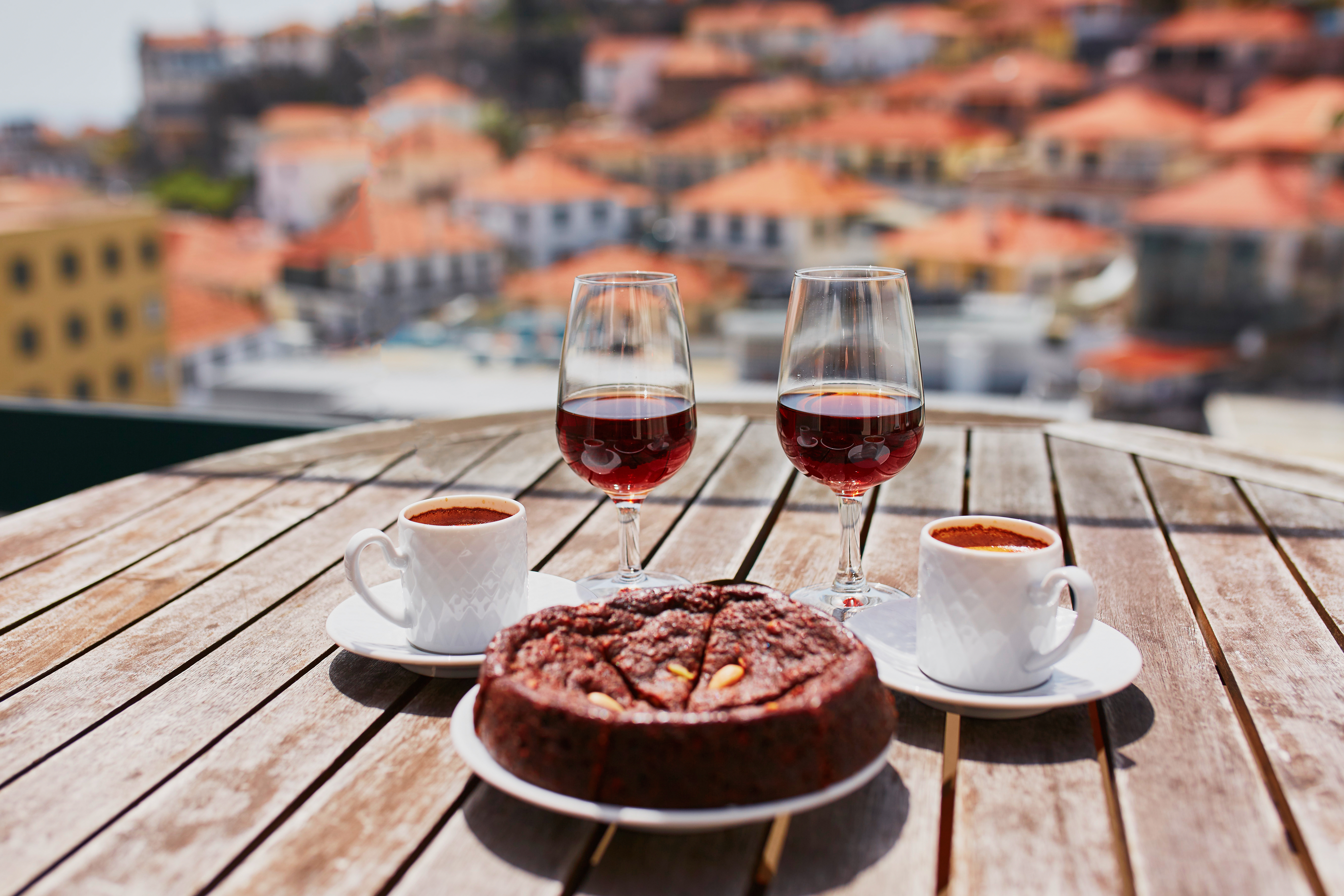 Two glasses of Madeira wine, two cups of fresh espresso coffee and traditional Portuguese honey and nut dessert bolo de mel in cafe