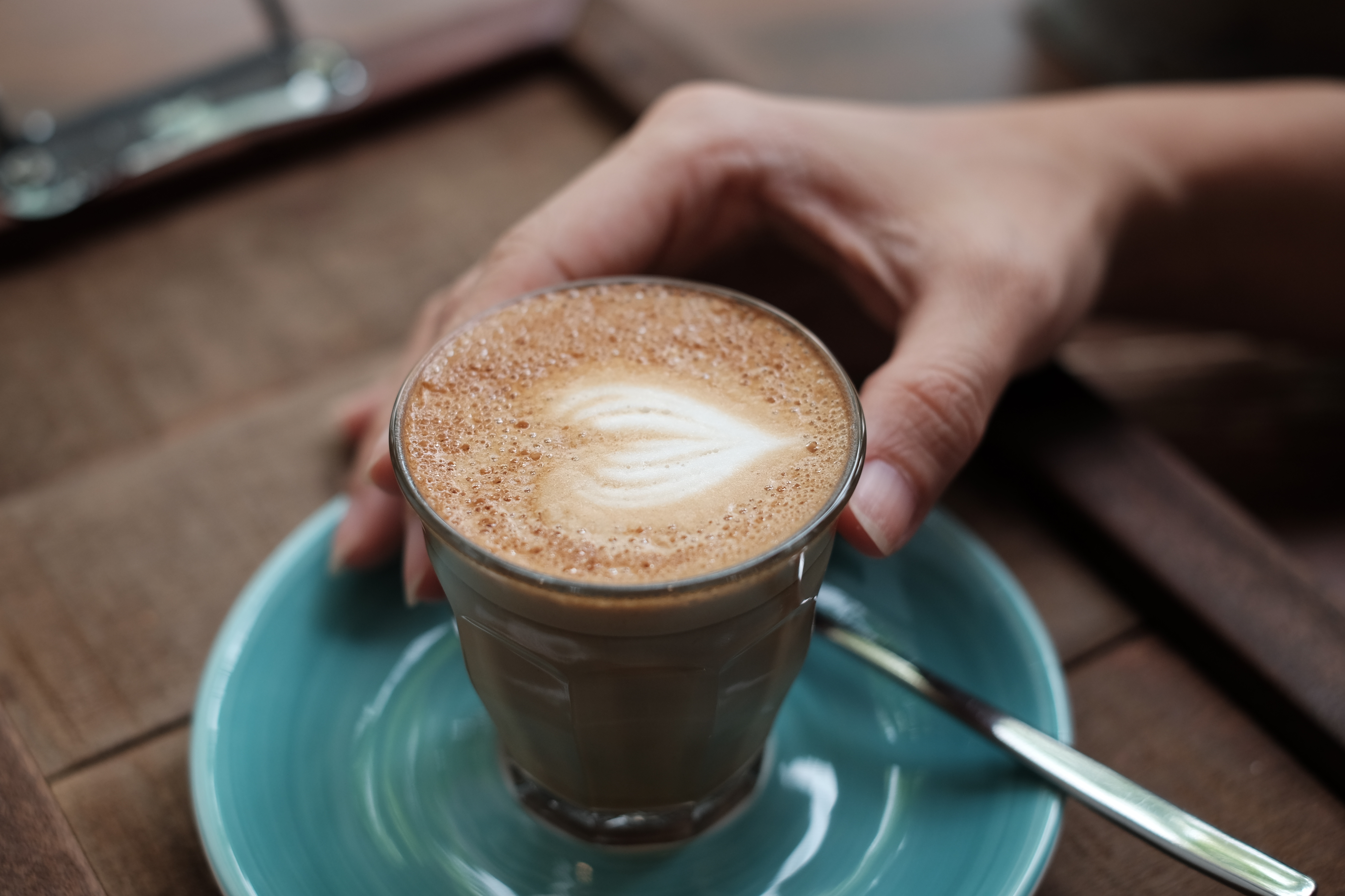 coffee latte art in coffee shop wood texture background with woman hand.Piccolo Latte Coffee on the wooden table background.