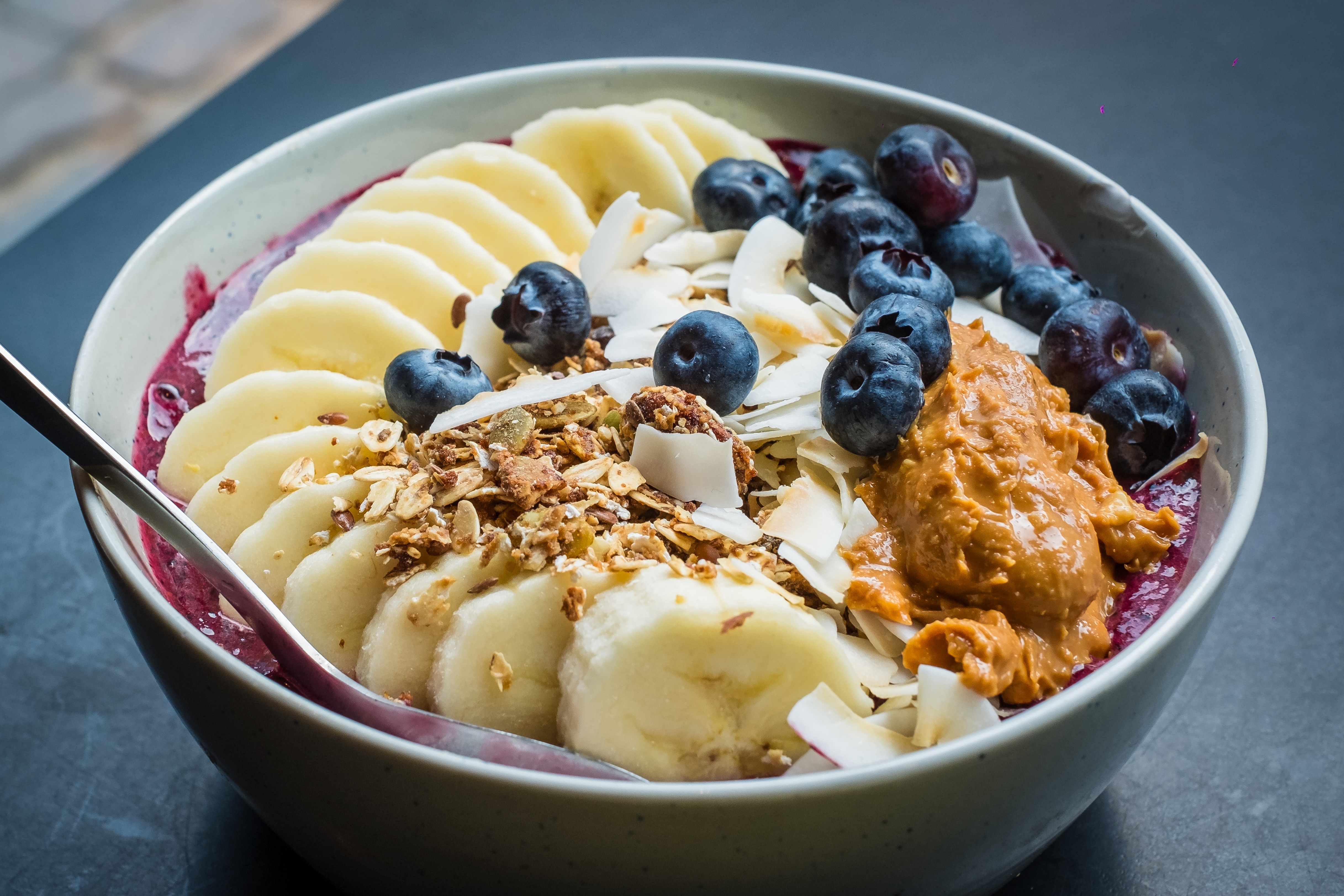 Smoothie bowl with acai powder, blueberries, peanut butter, banana, roasted coconut flakes and granola. Healthy balanced breakfast bowl.