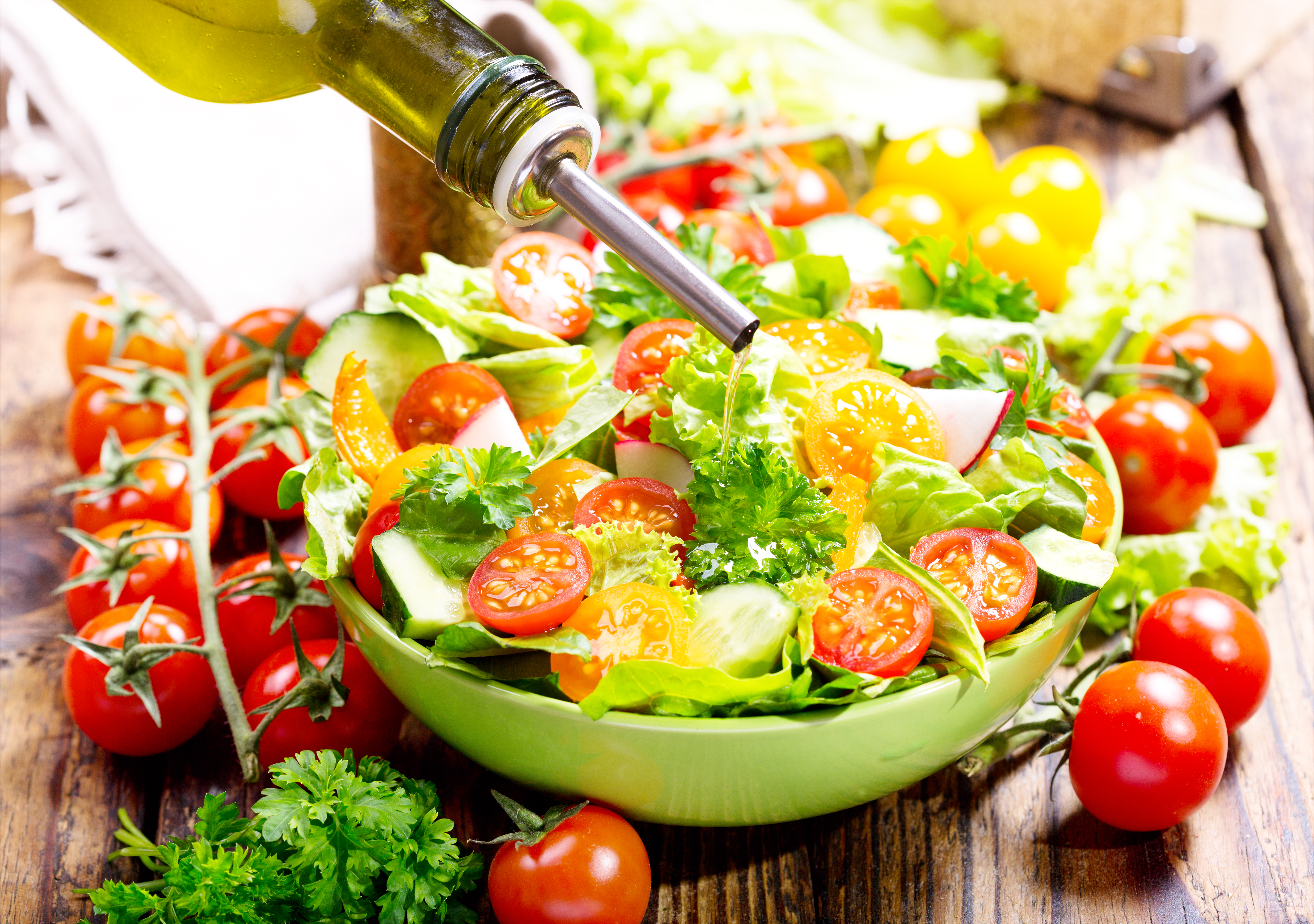 pouring oil into bowl of salad with vegetables