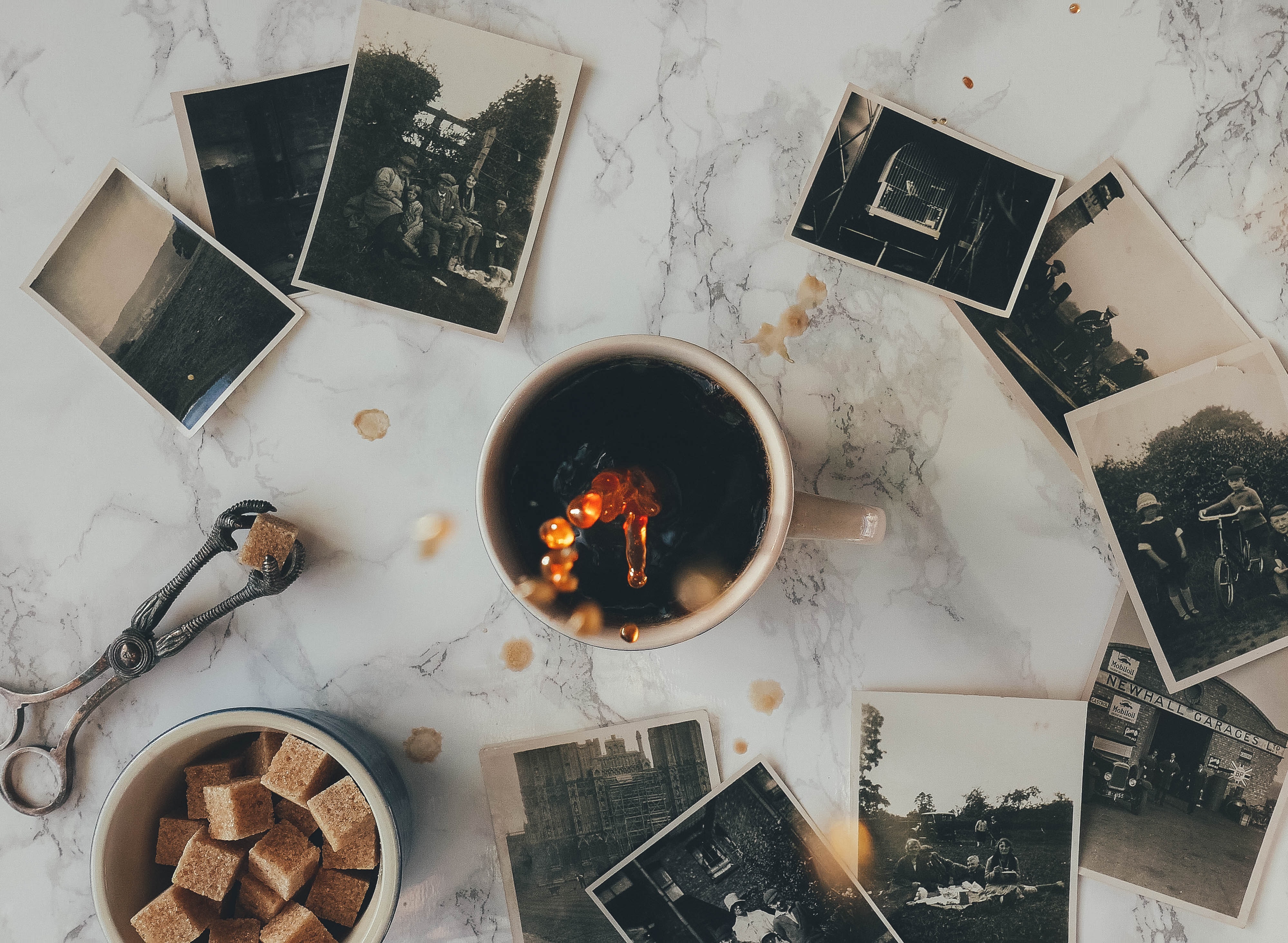cup of coffee, sugar cubes and old photos on a marble countertop