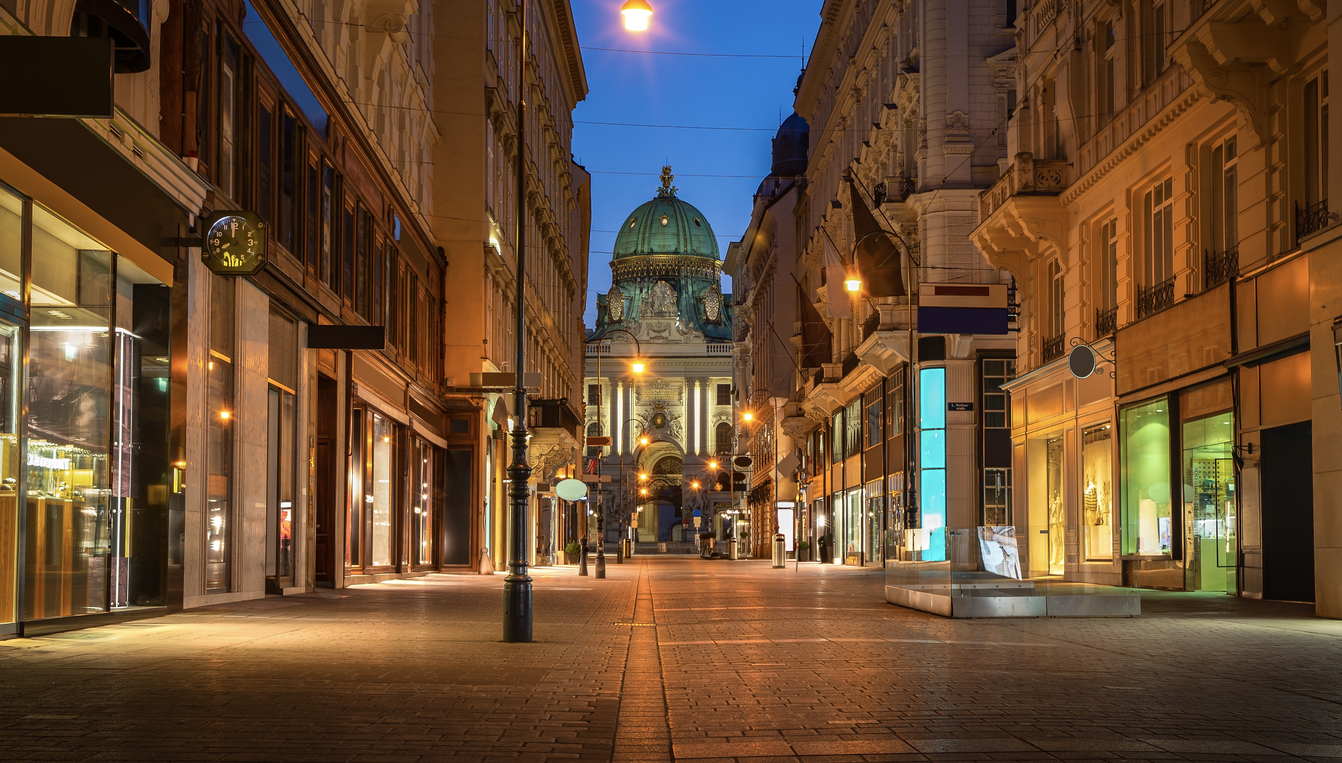 Shopping street in Vienna (Kolhmarkt) leading to historical palace Hofburg during evening with street lights