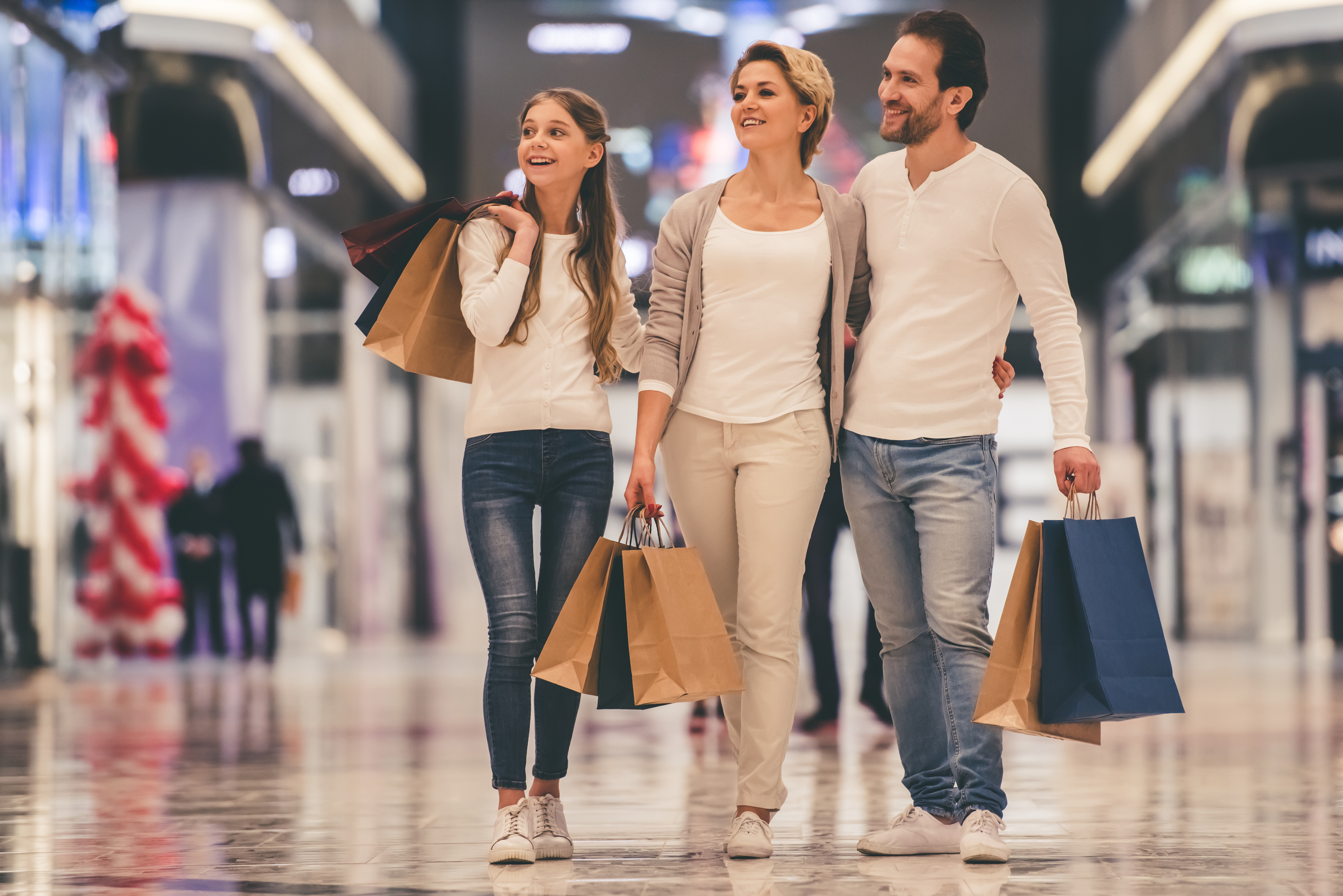 Beautiful parents and their daughter are holding shopping bags and smiling while doing shopping in mall