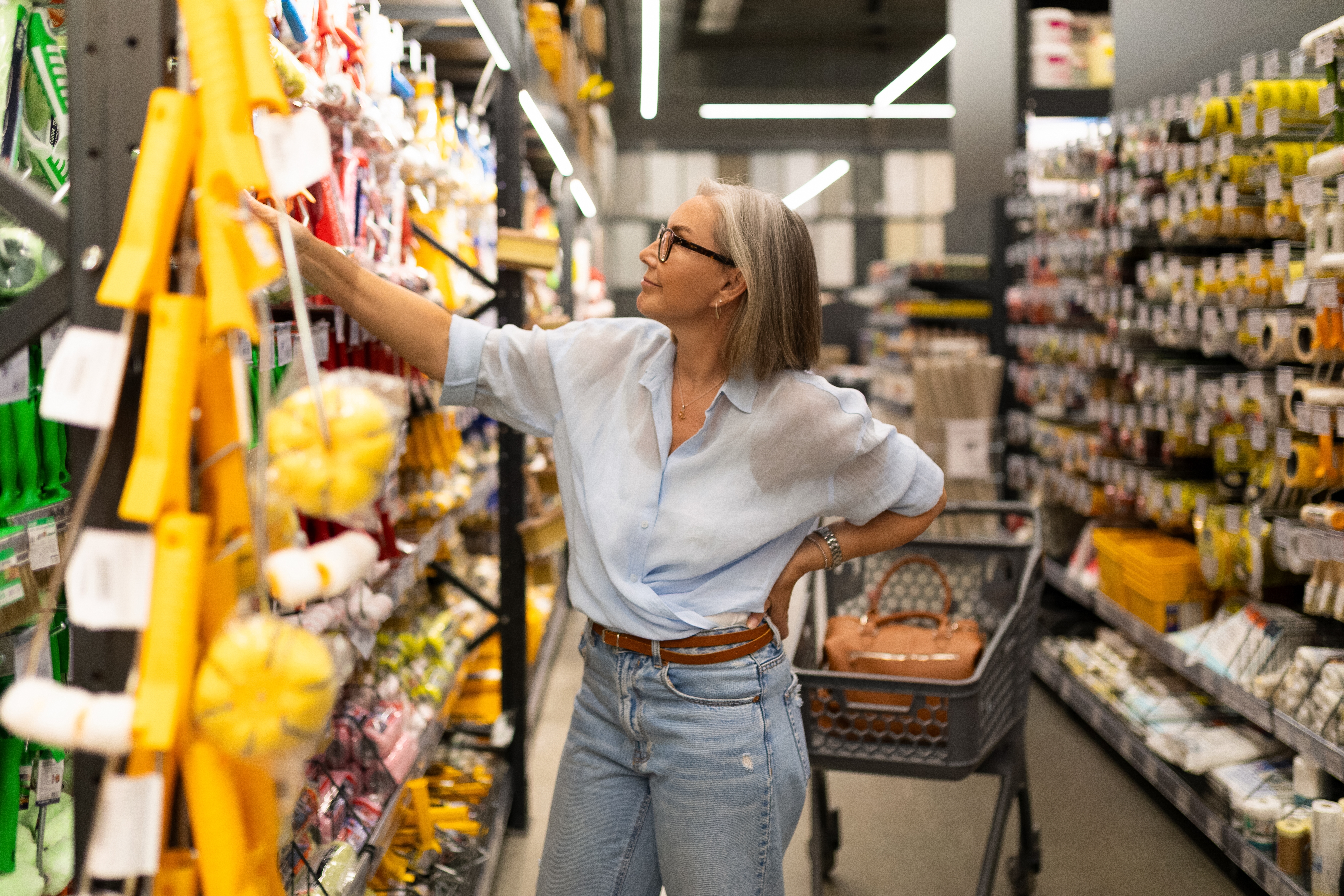 A woman browses through a wide selection of home improvement products in a well-stocked retail store. She examines items related to kitchen, gardening, and tools while shopping.