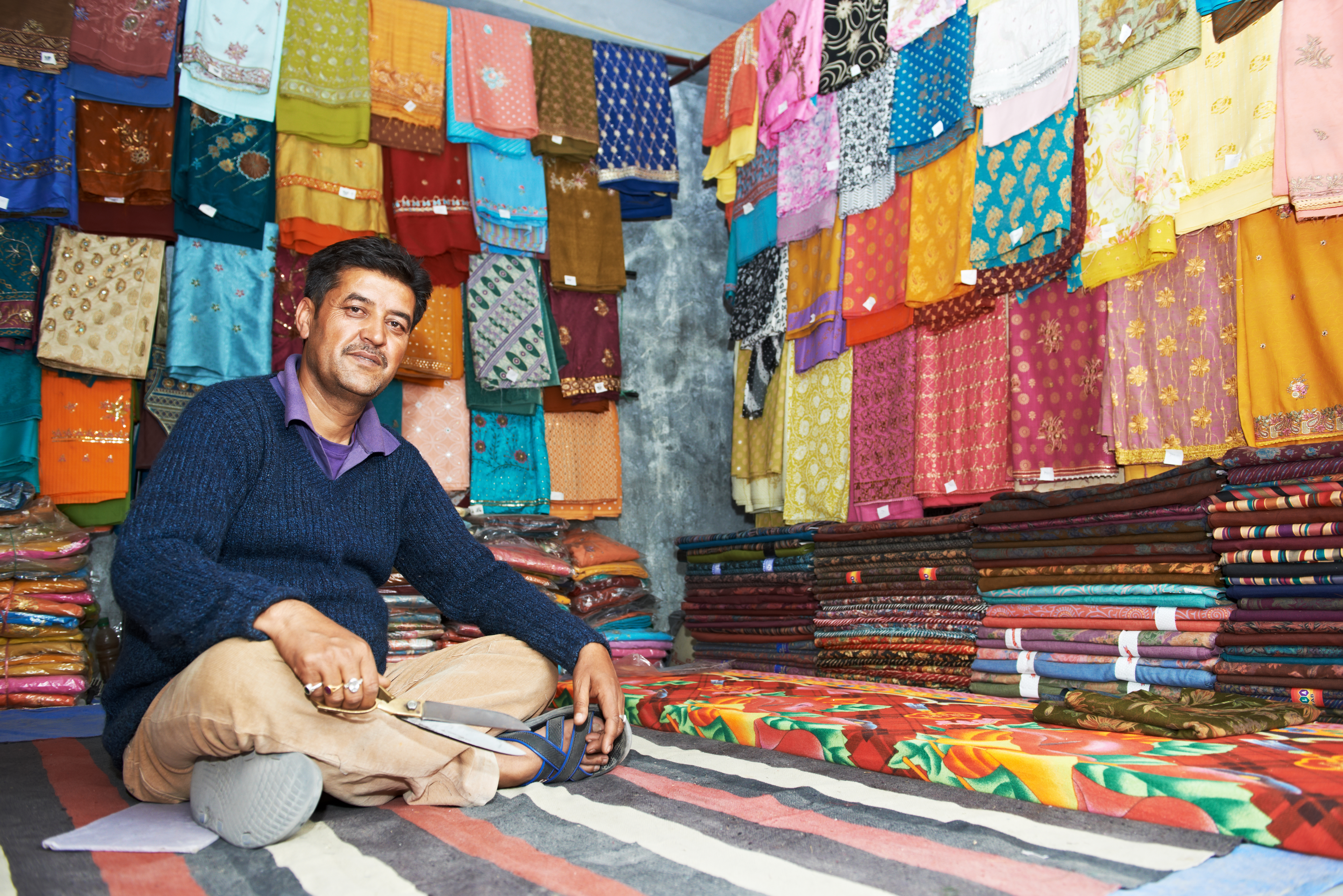 small shop owner indian man selling shawls, clothing and souvenirs at his store