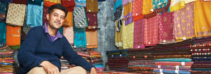 small shop owner indian man selling shawls, clothing and souvenirs at his store