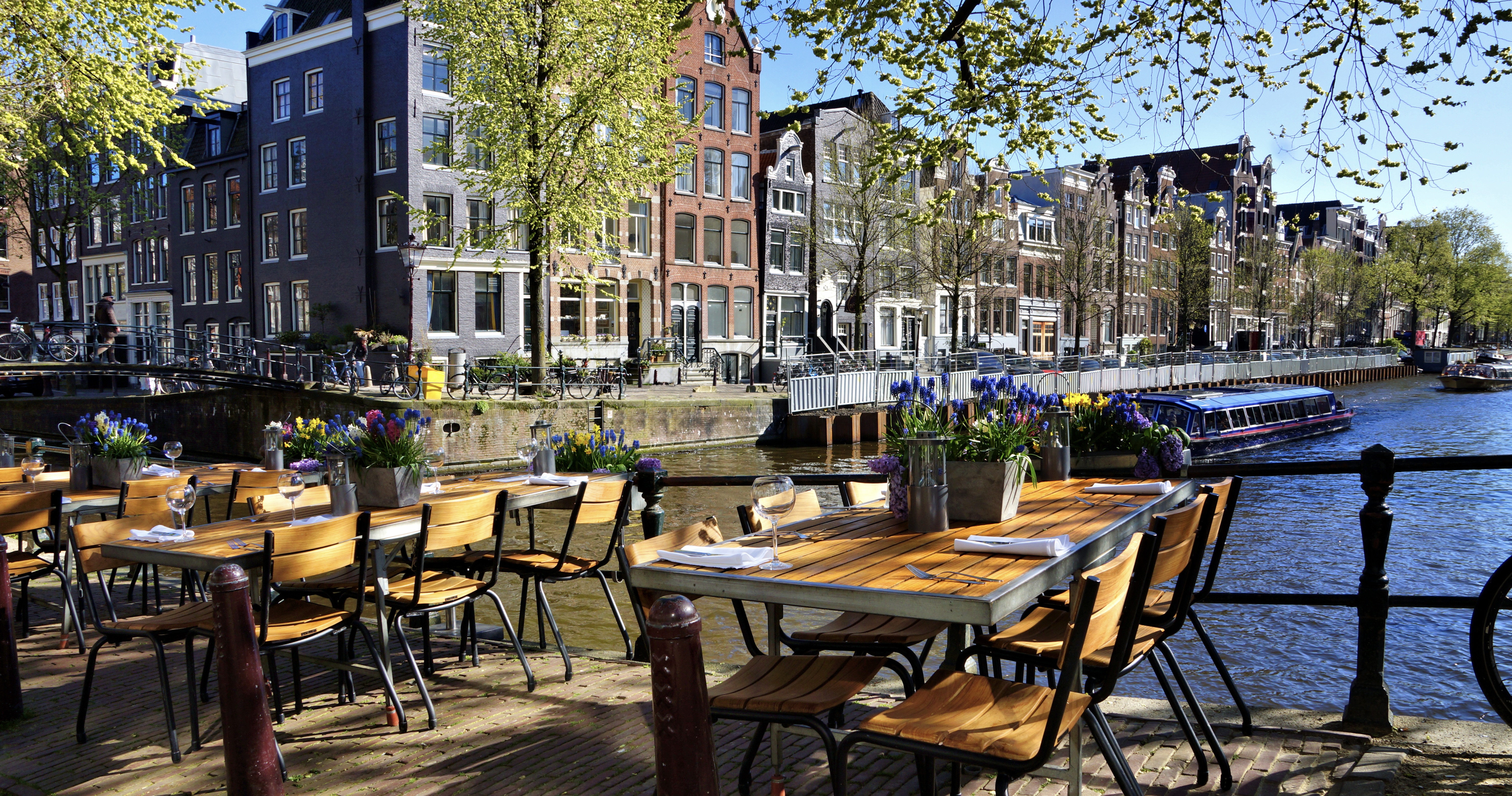 Restaurant tables lining the beautiful canals of Amsterdam under blue skies during springtime, Netherlands