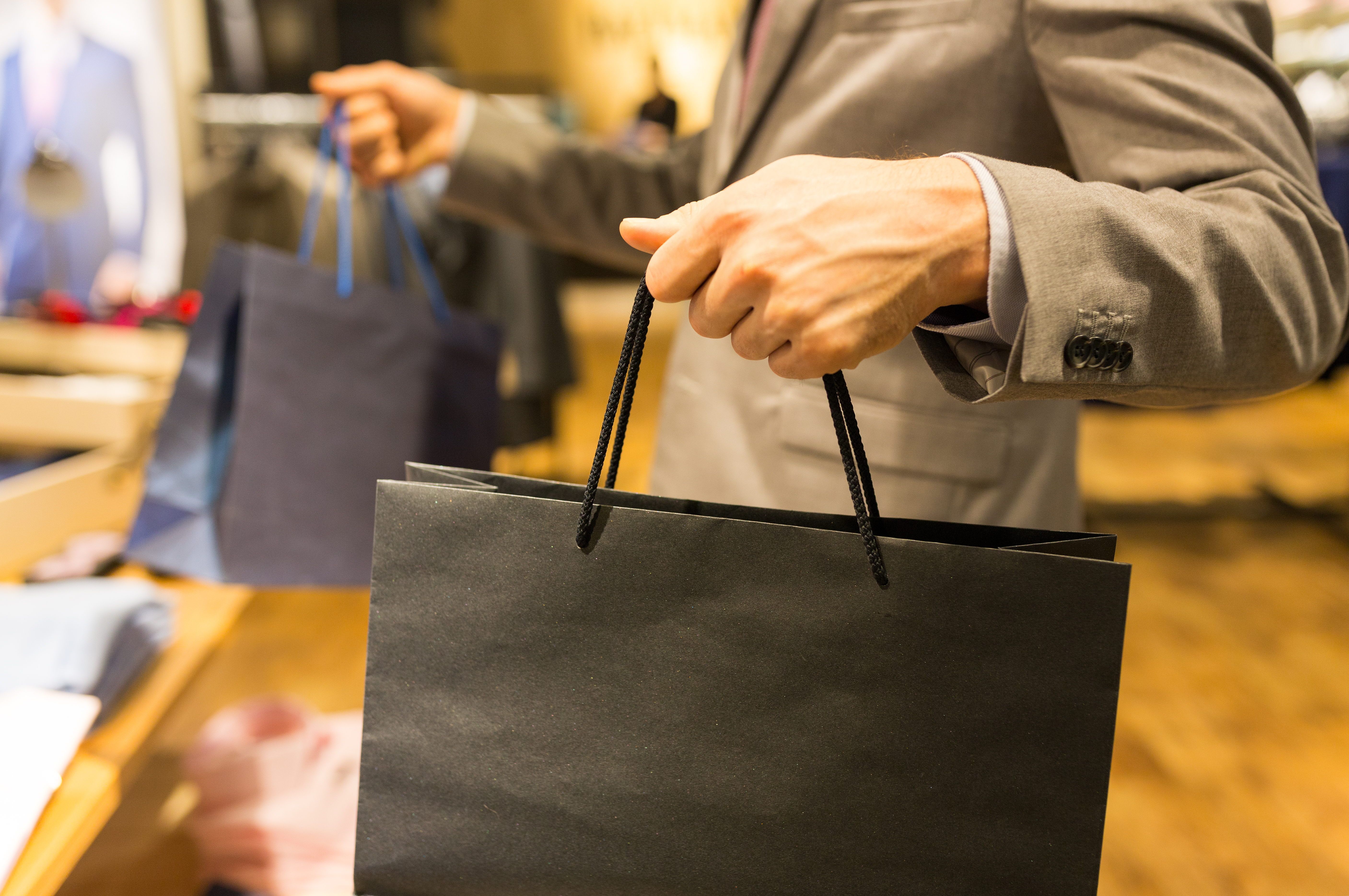 sale, fashion, retail, business style and people concept - close up of man in suit with shopping bags at clothing store