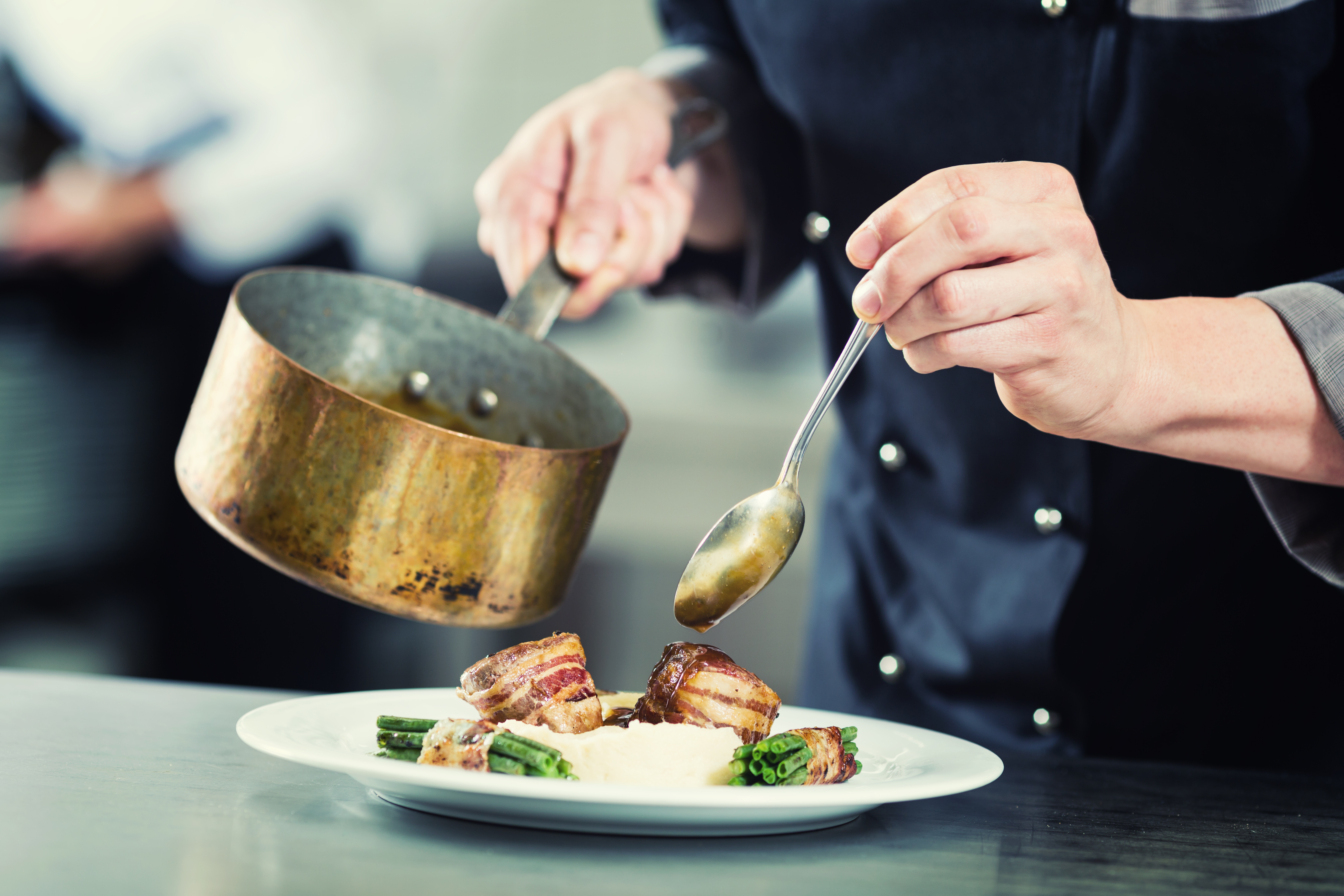 Chef pouring sauce on dish in restaurant kitchen, crop on hands, filtered image