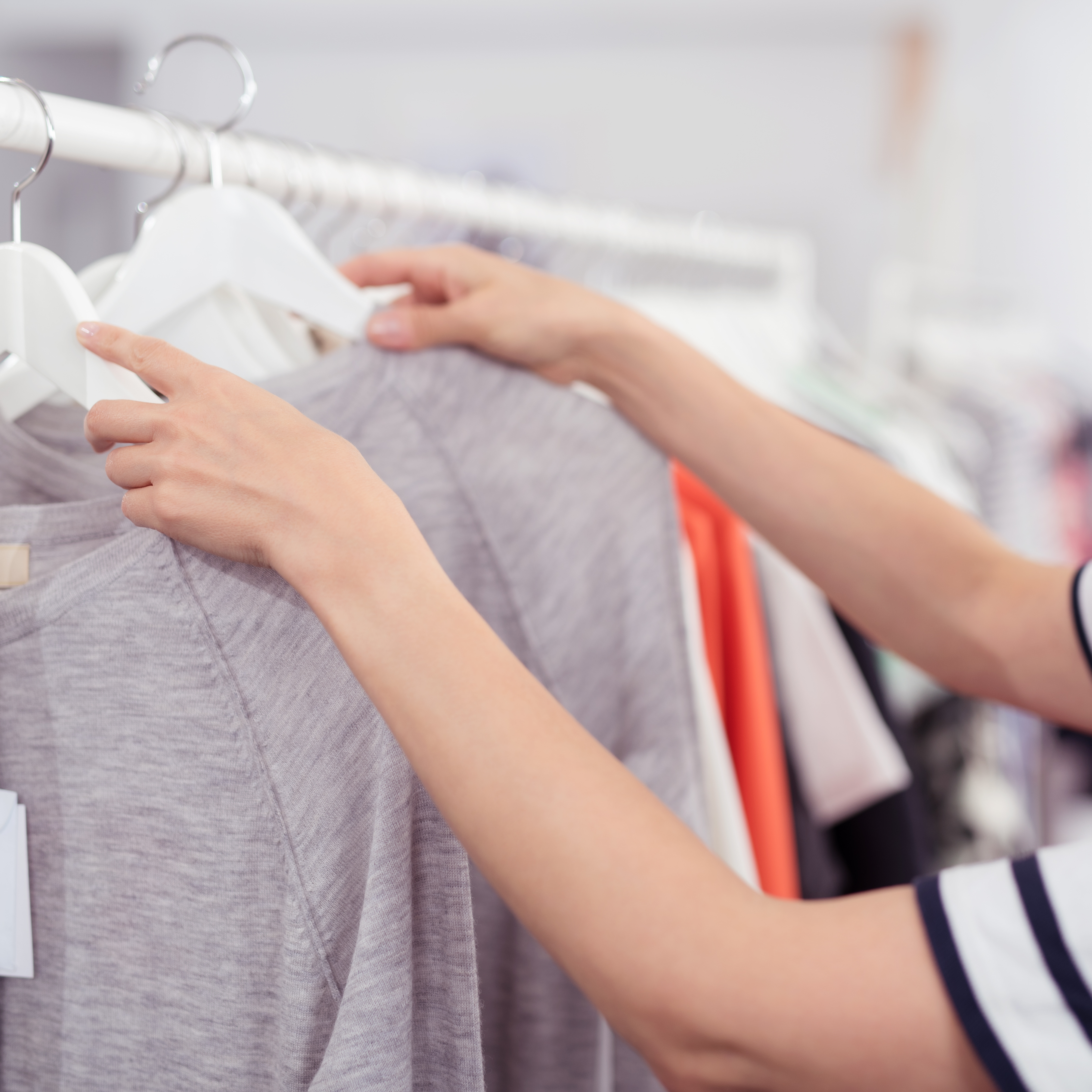 Close up Hands of a Woman Rummaging Trendy Clothes Hanging on the Rail Inside a Clothing Store