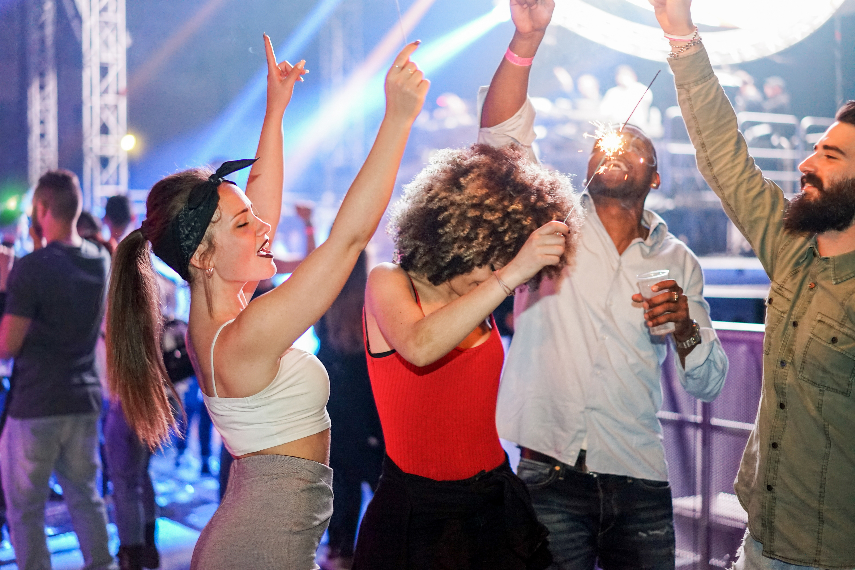 Young friends dancing in night club festival event party with dj in background - Happy people having fun inside disco - Nightlife concept - Unfiltered photo with soft focus on left girl face