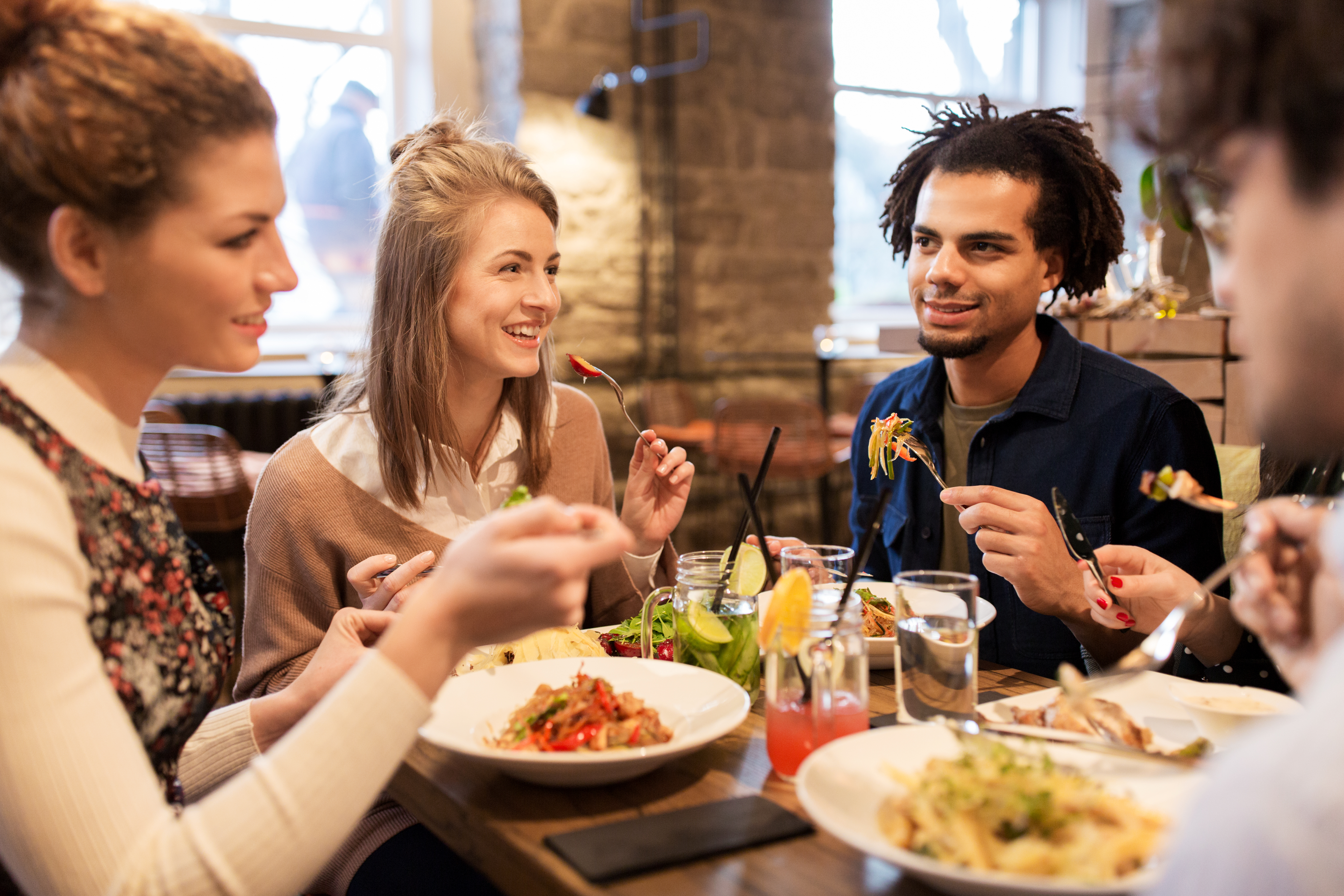 leisure, food, drinks, people and holidays concept - happy friends eating and drinking at restaurant