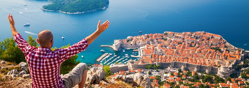 man with opened arms sitting on the edge of a cliff, looking down to the Old Town of Dubrovnik, Croatia