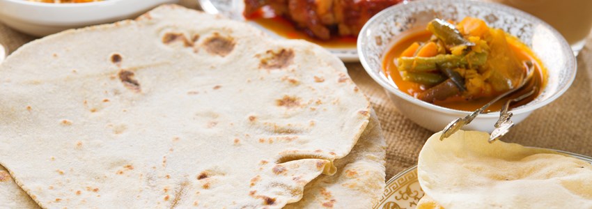 Chapatti roti or Flat bread, curry chicken, biryani rice, salad, masala milk tea and papadom. Indian food on dining table.