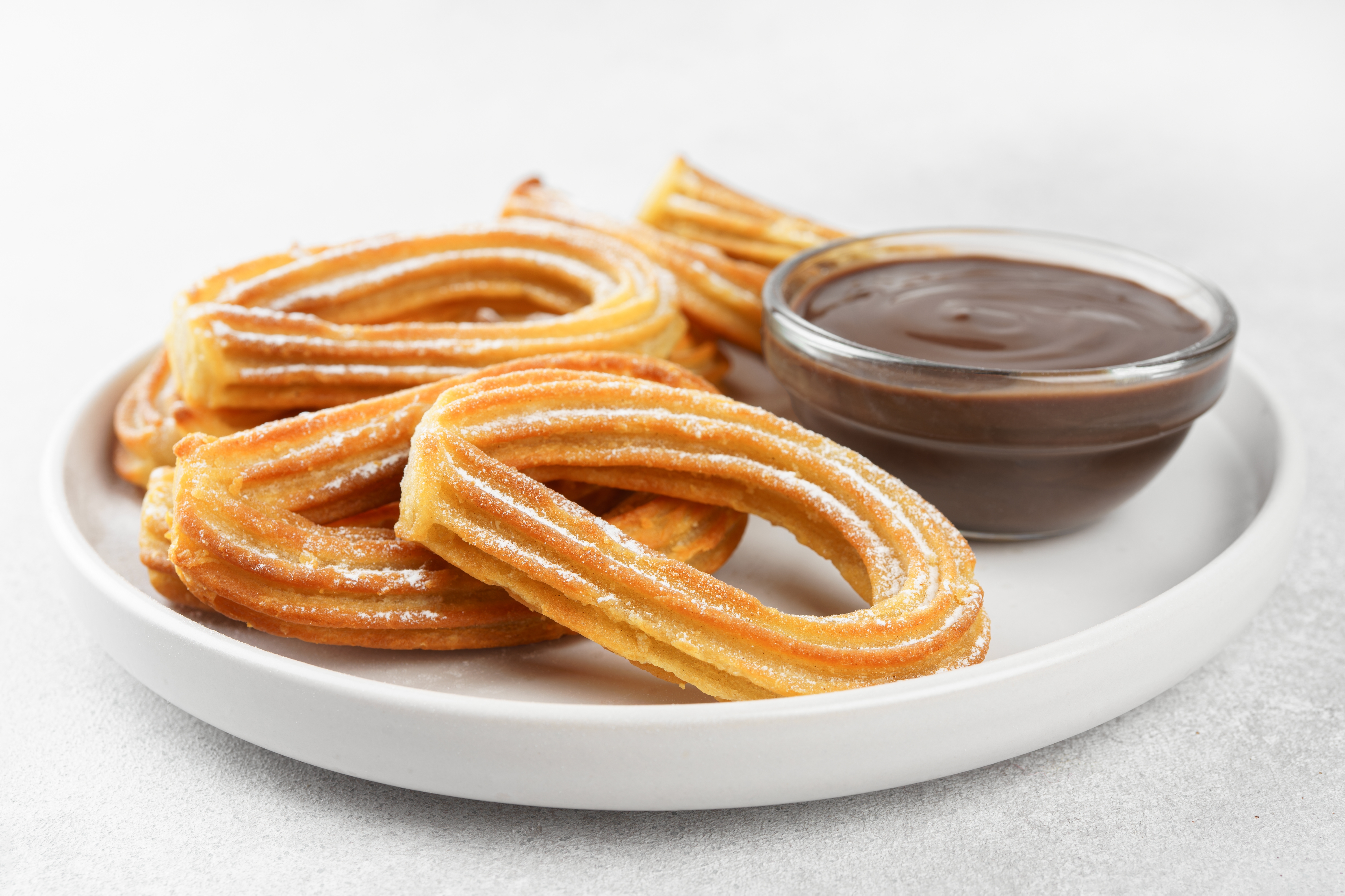Traditional spanish dessert churros, fried dough pastry dusted with powdered sugar and chocolate sause on white background.