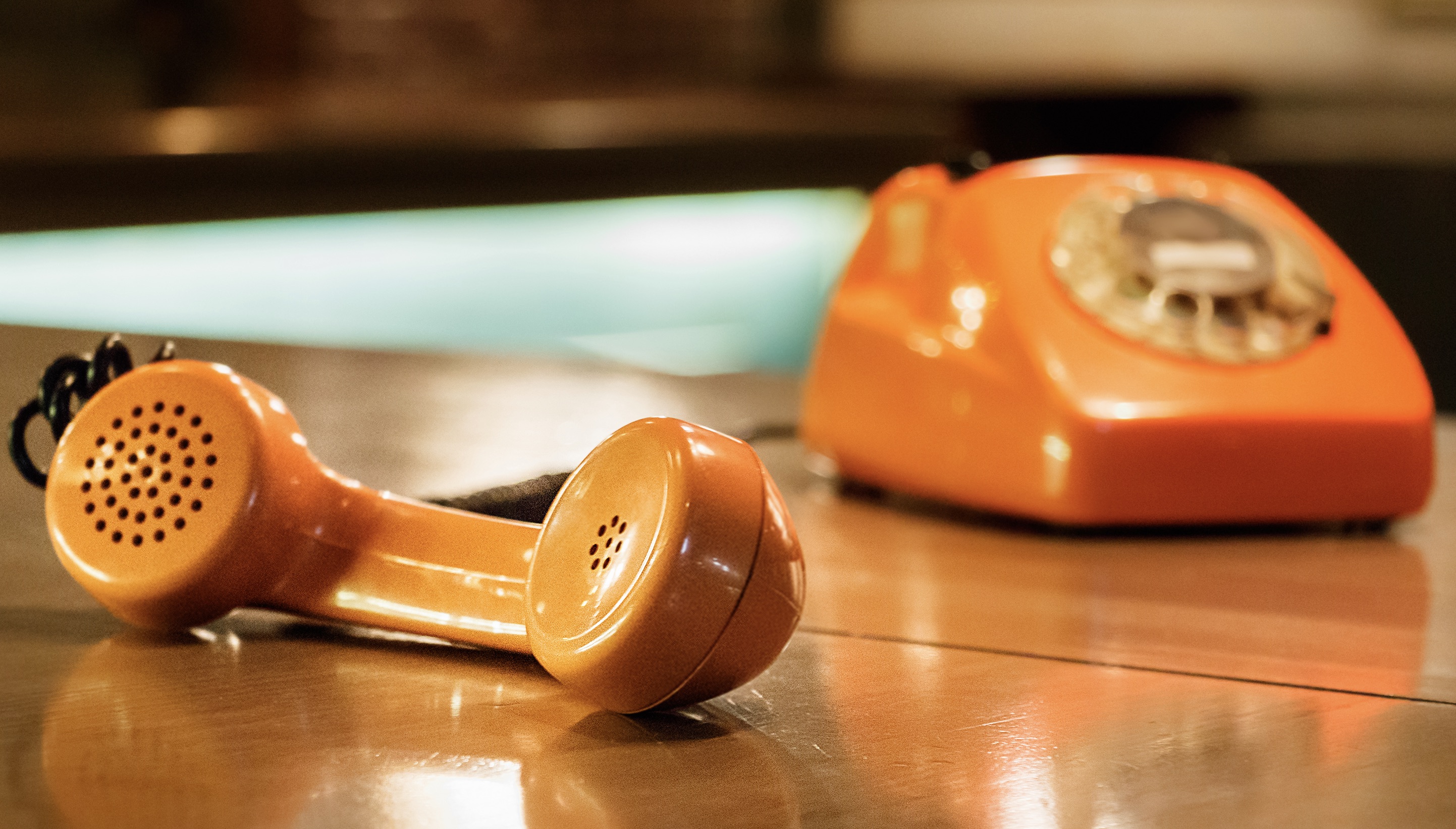 Handset of an orange telephone with dial placed on a wooden table inside a bar.
