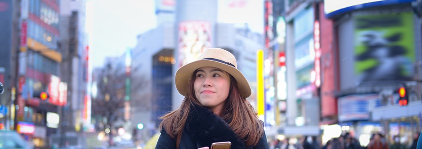 Woman tourist is using smart phone at Shibuya cross walk junction.