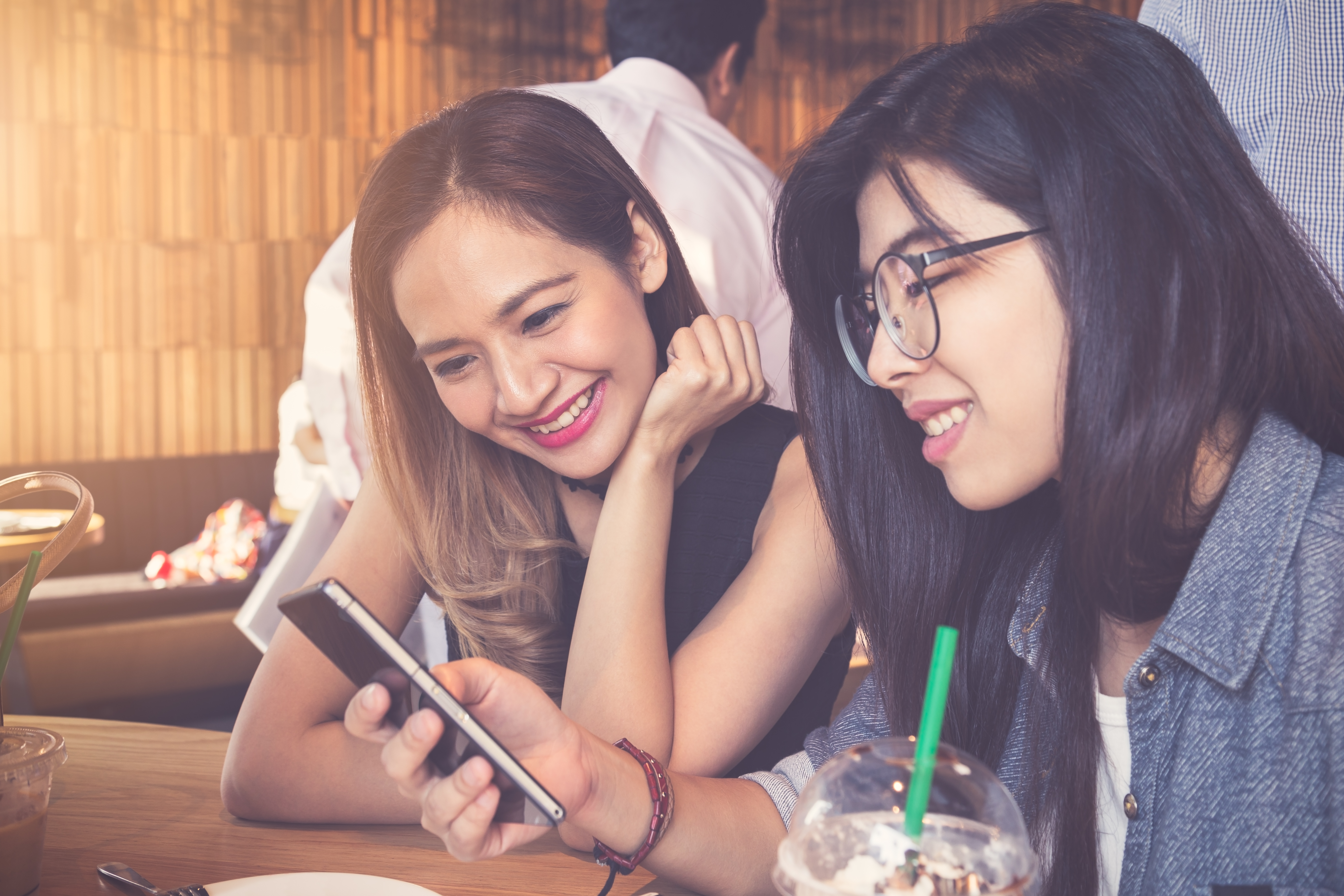 Two young woman enjoy using mobile smartphone in coffee cafe, technology lifestyles