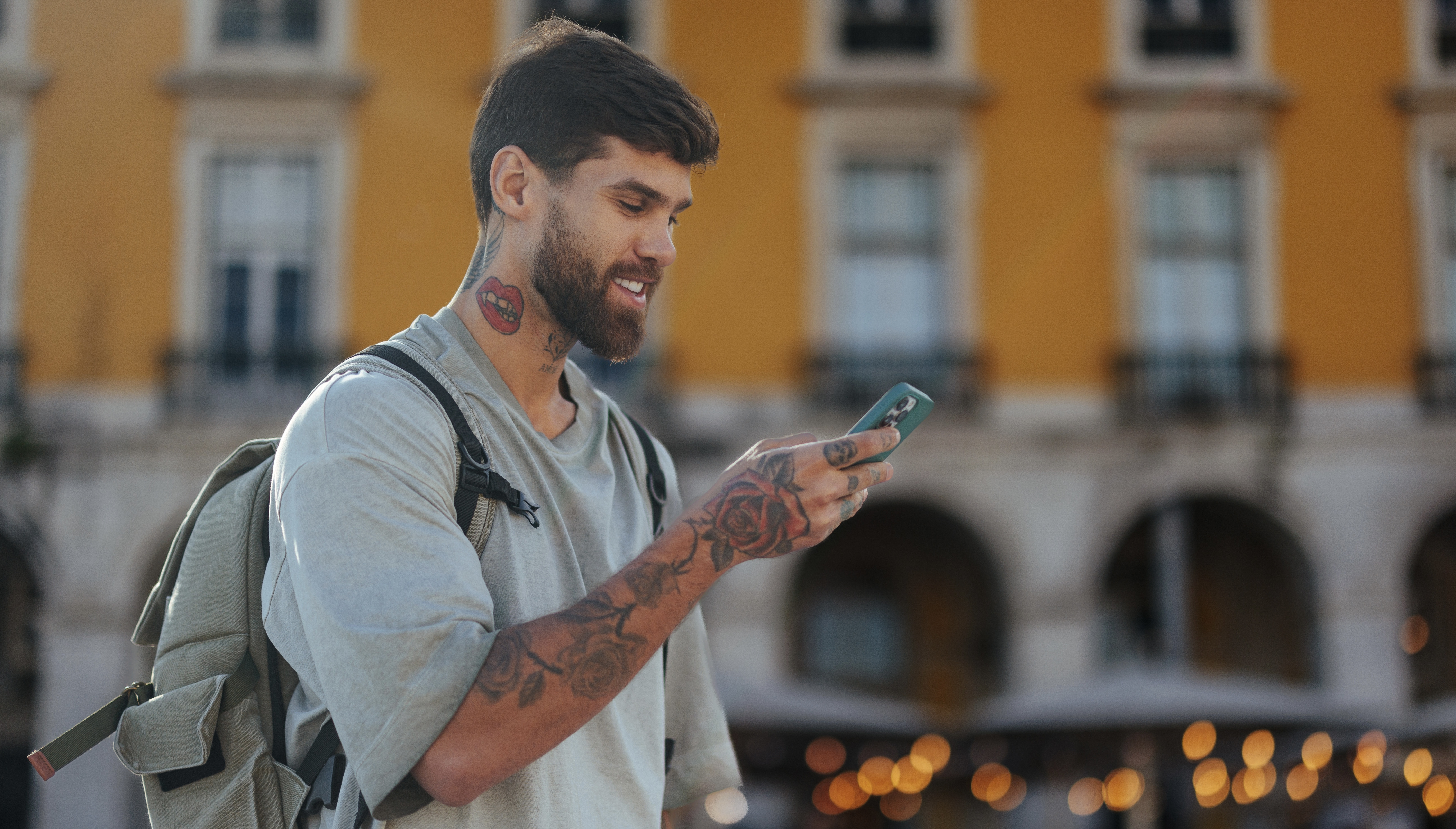 Young man with tattoos and backpack using mobile phone in commerce square, lisbon, portugal