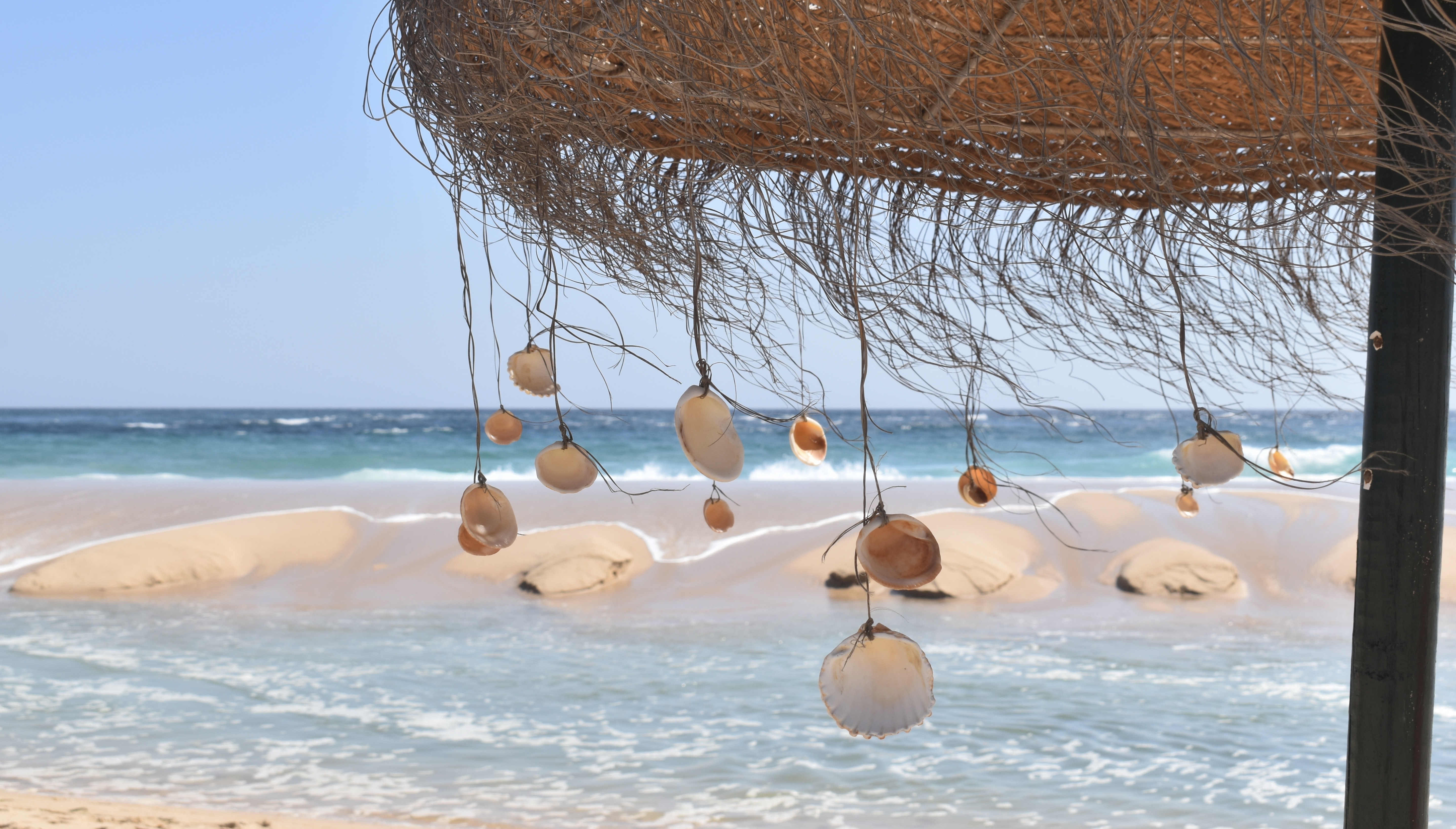 Beach life in the Algarve. Ilha Deserta. The ocean, the beach and an umbrela with seashells.