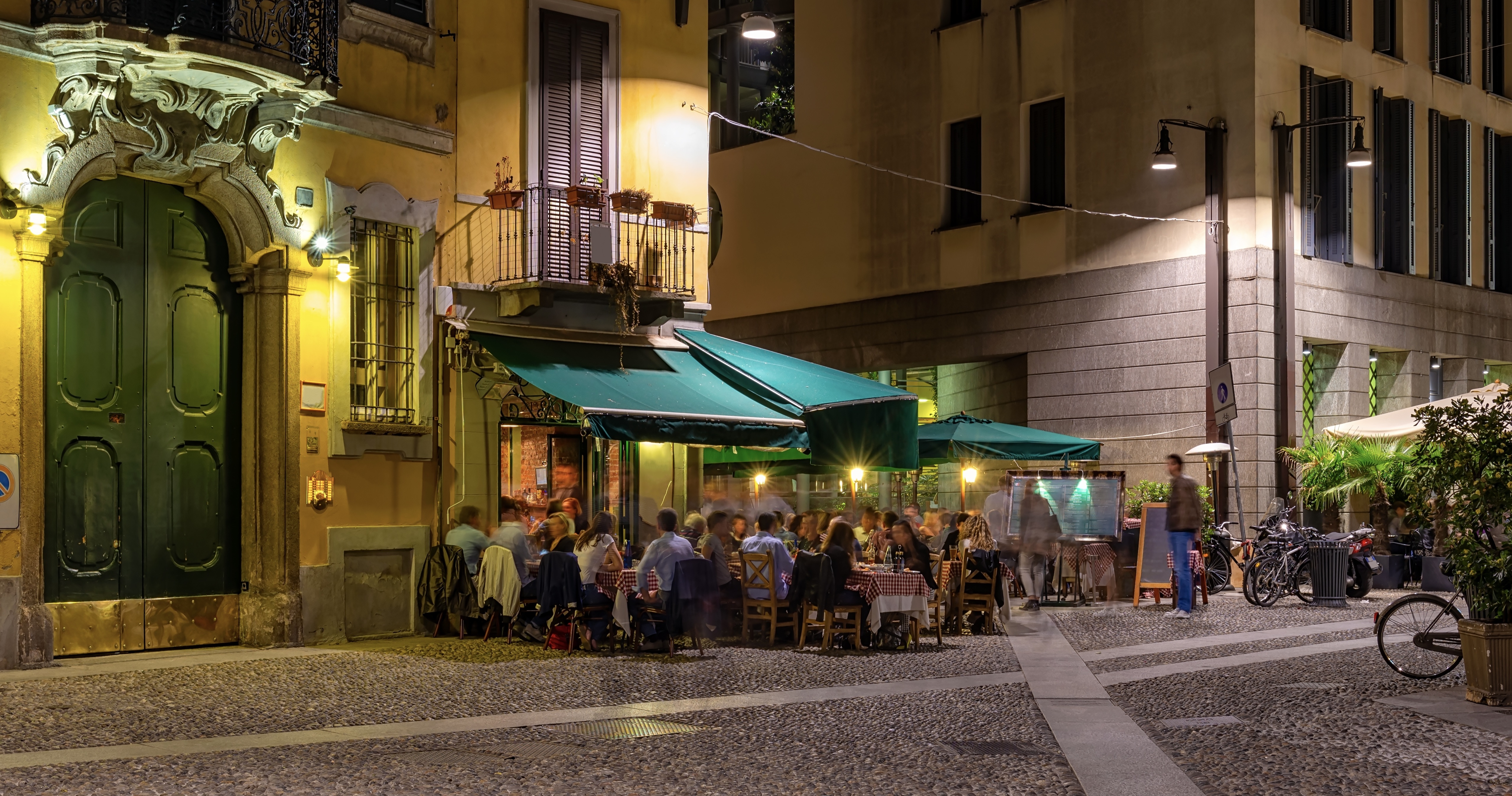 Old street with restaurant tables Milan, Italy. Night cityscape of Milan