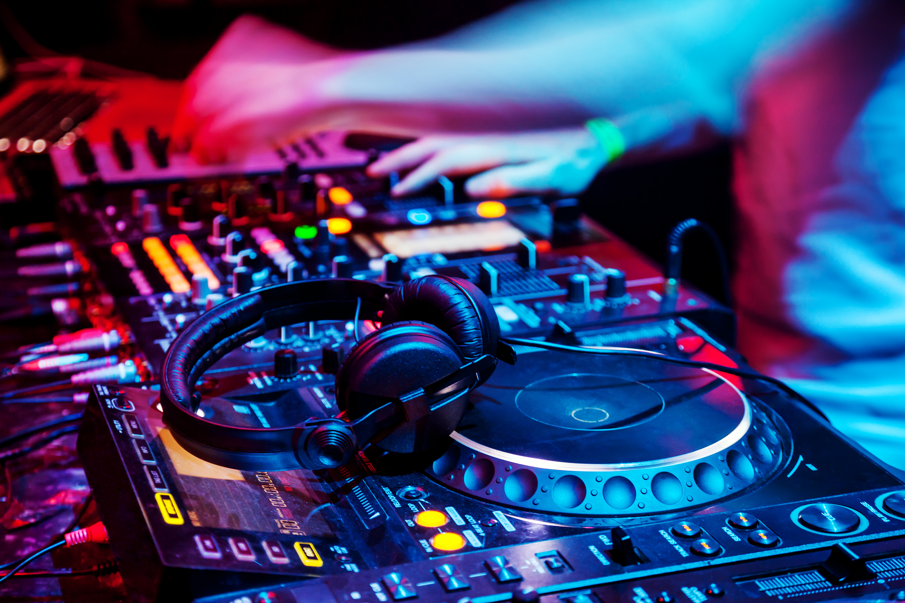 Dj mixes the track in the nightclub at party. Headphones in foreground and DJ hands in motion