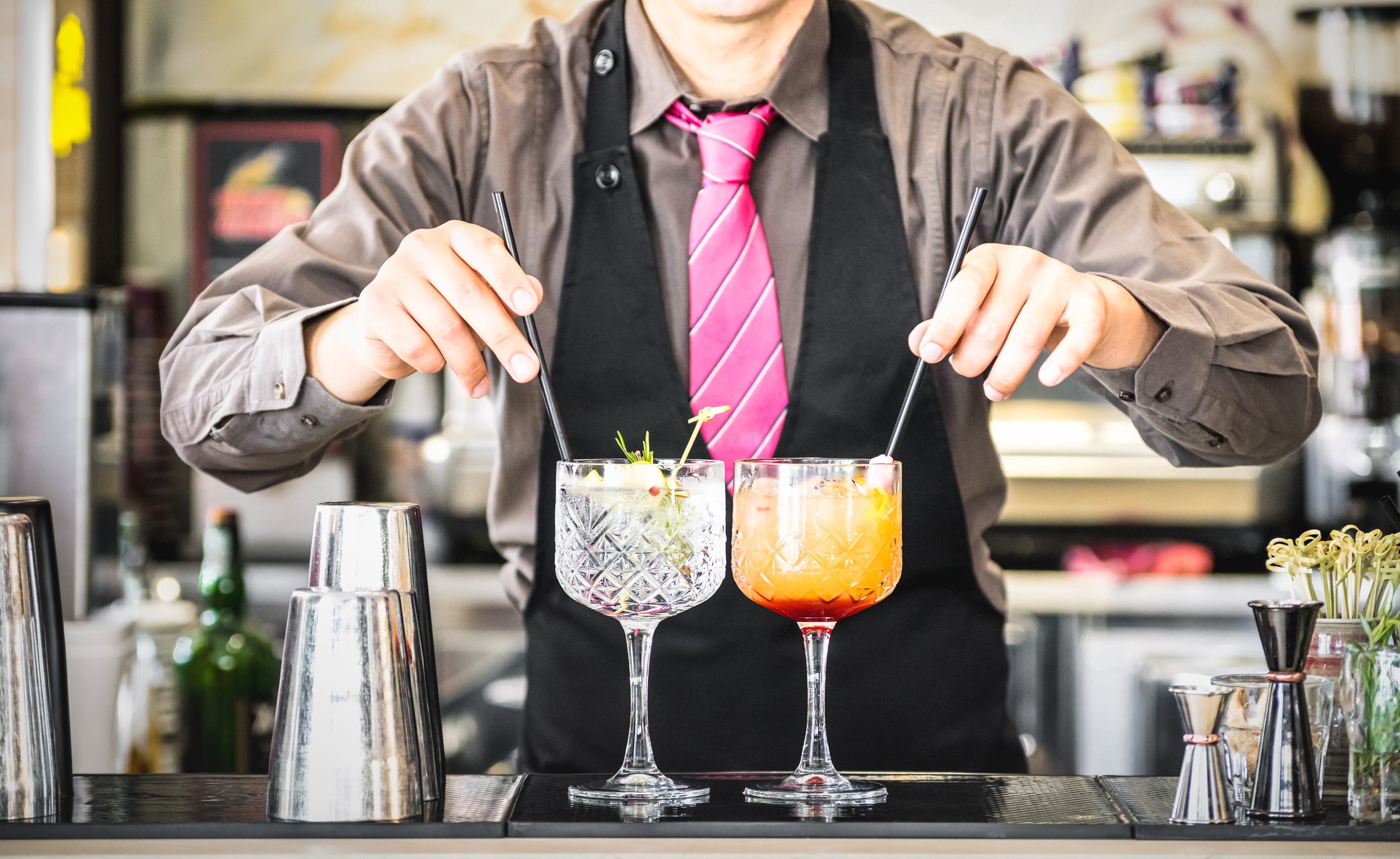 Classic bartender serving gin tonic and tequila sunrise with straw on drink glasses cups at fashion cocktail bar - Food and beverage concept with professional barman working at mixology restaurant